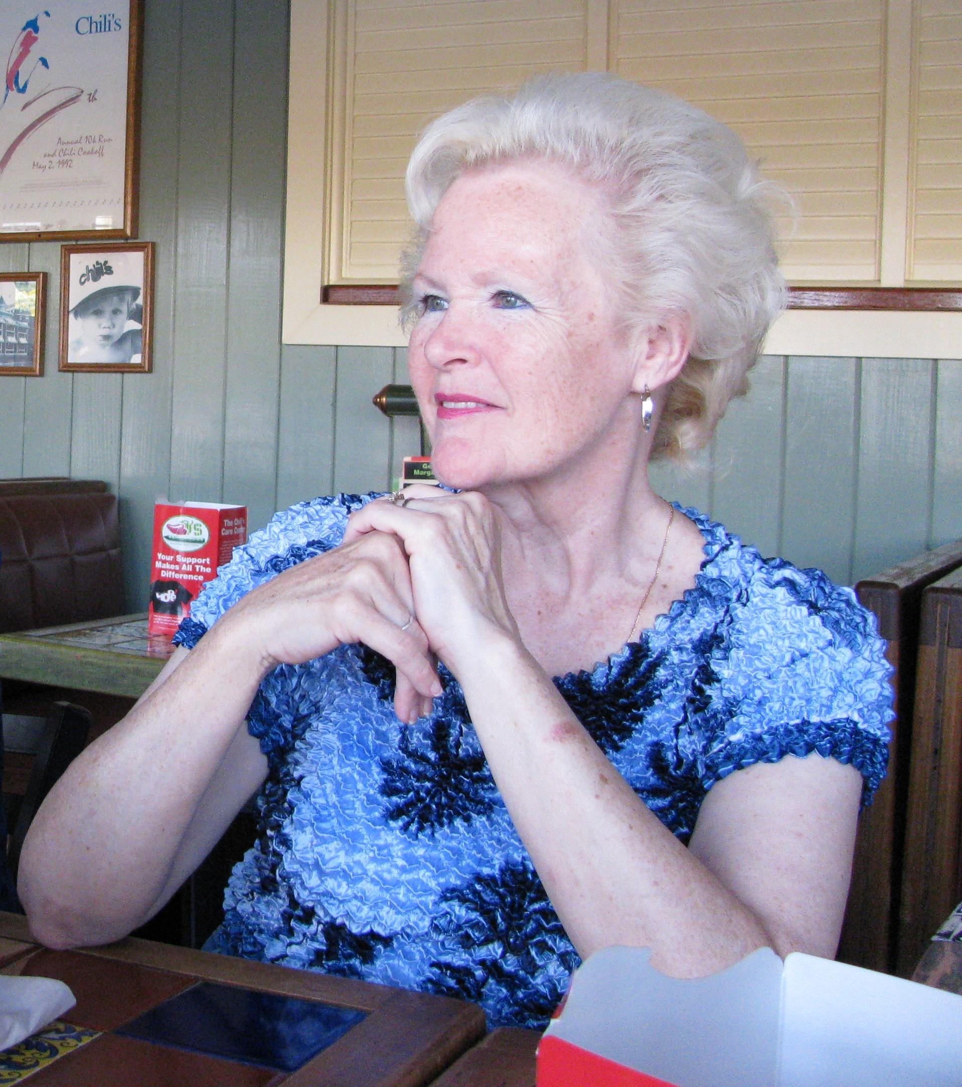 A thoughtful woman with stylish hair sits at a restaurant table, reflecting on her surroundings.
