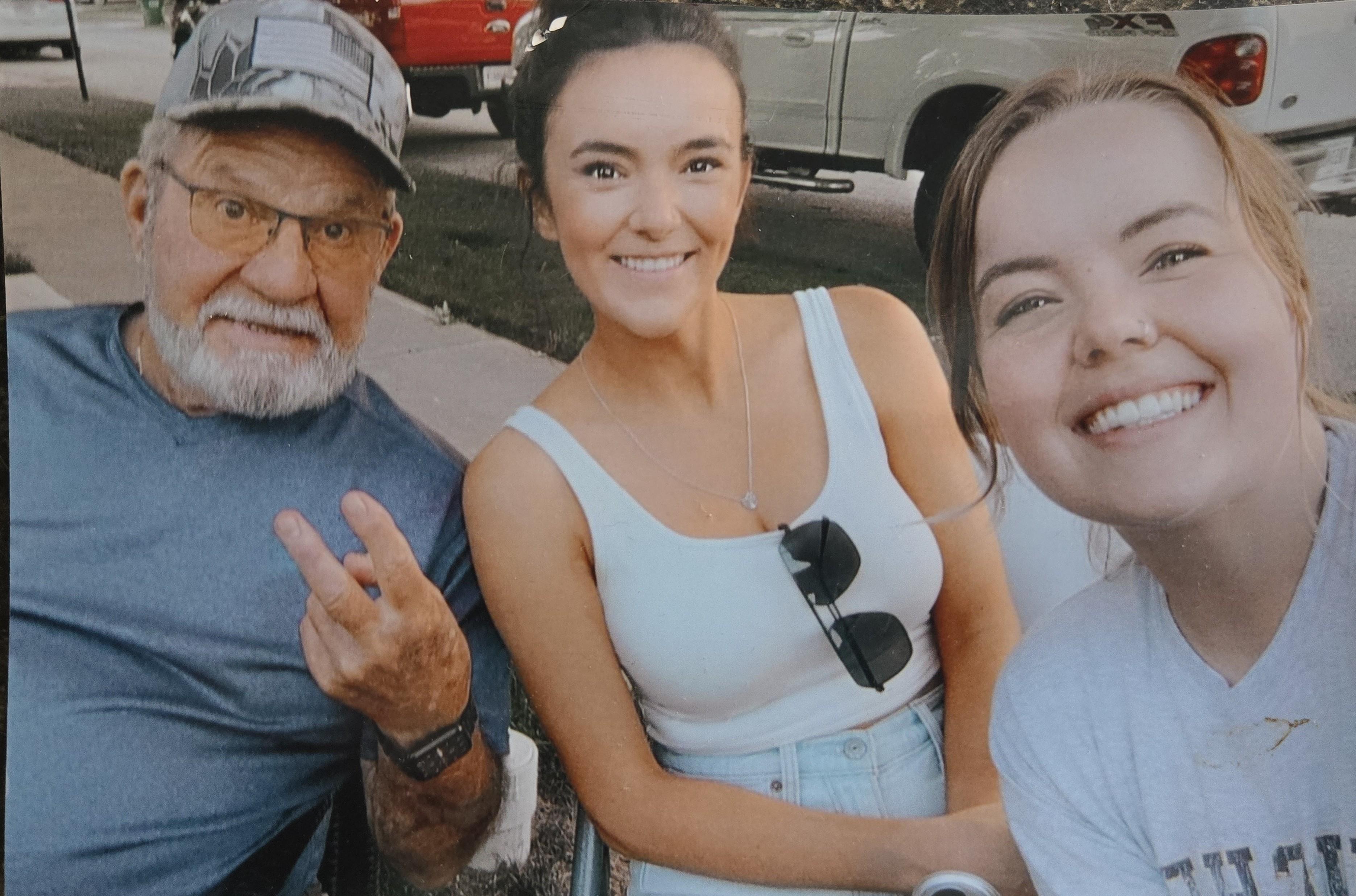 Two women and an elderly man smile and strike a pose for a selfie during a relaxed gathering.