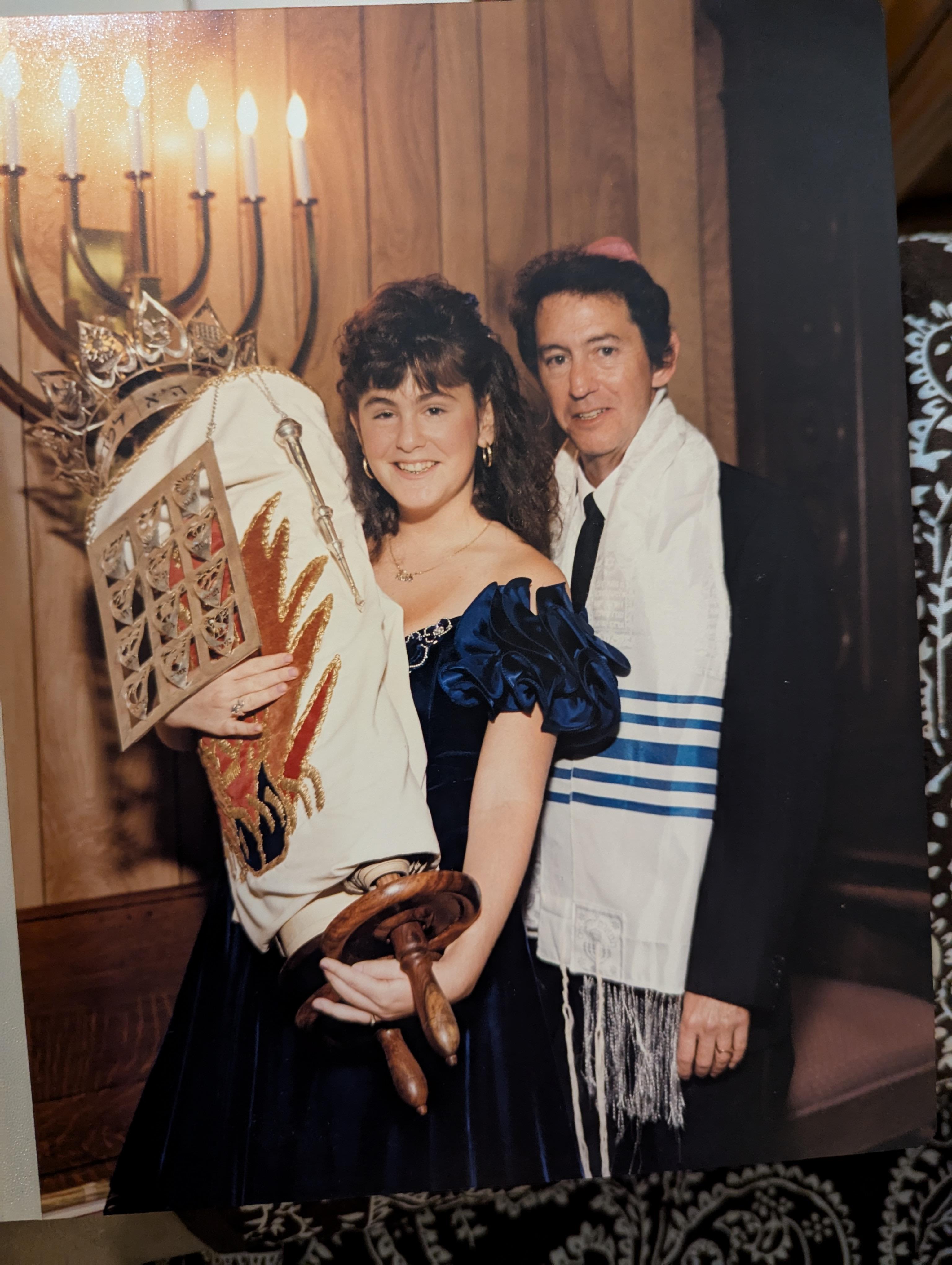 A woman in a formal dress and a man in traditional attire celebrate with a Torah.