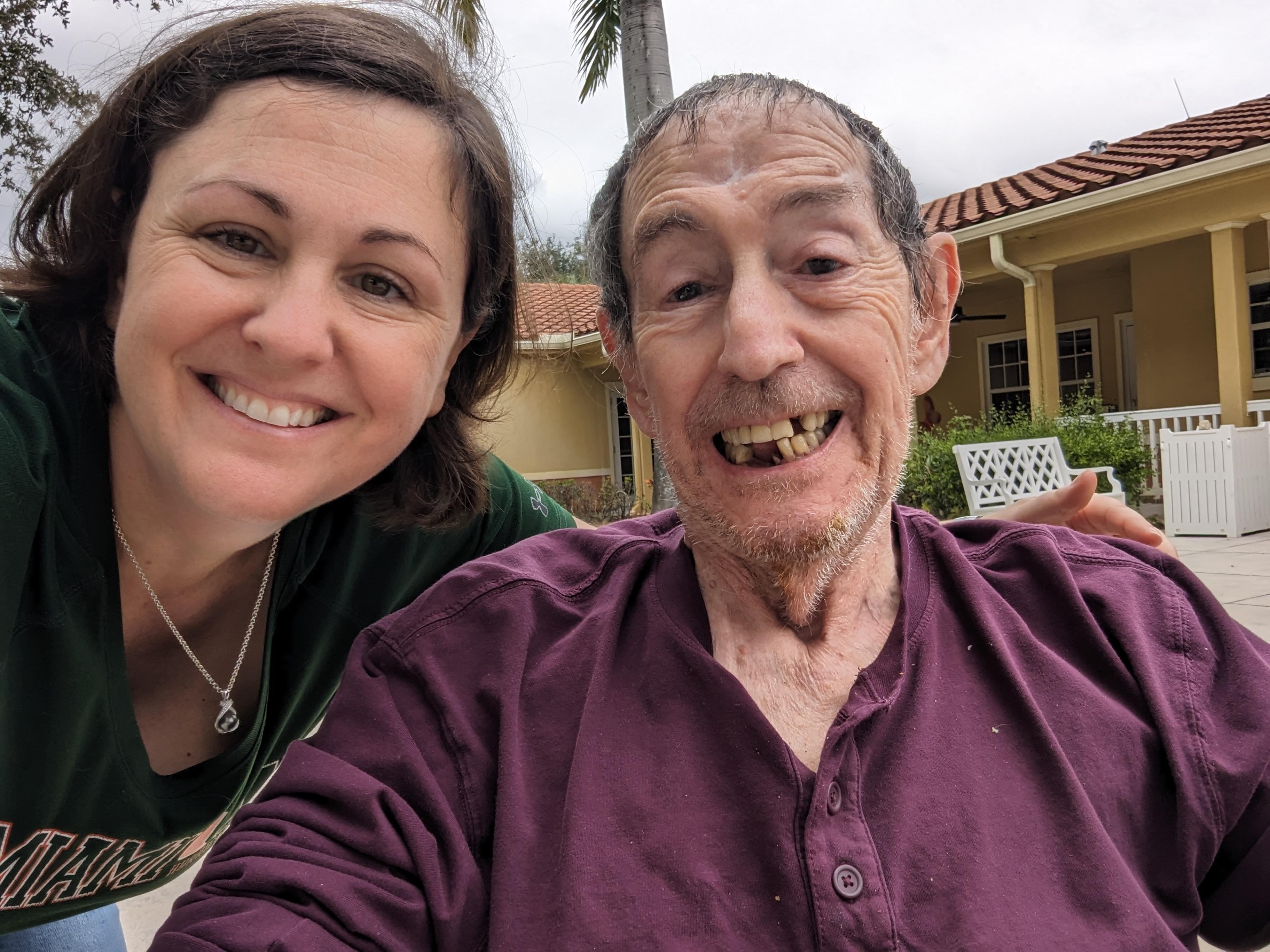 Woman and elderly man pose happily outside at a retirement community during daytime.