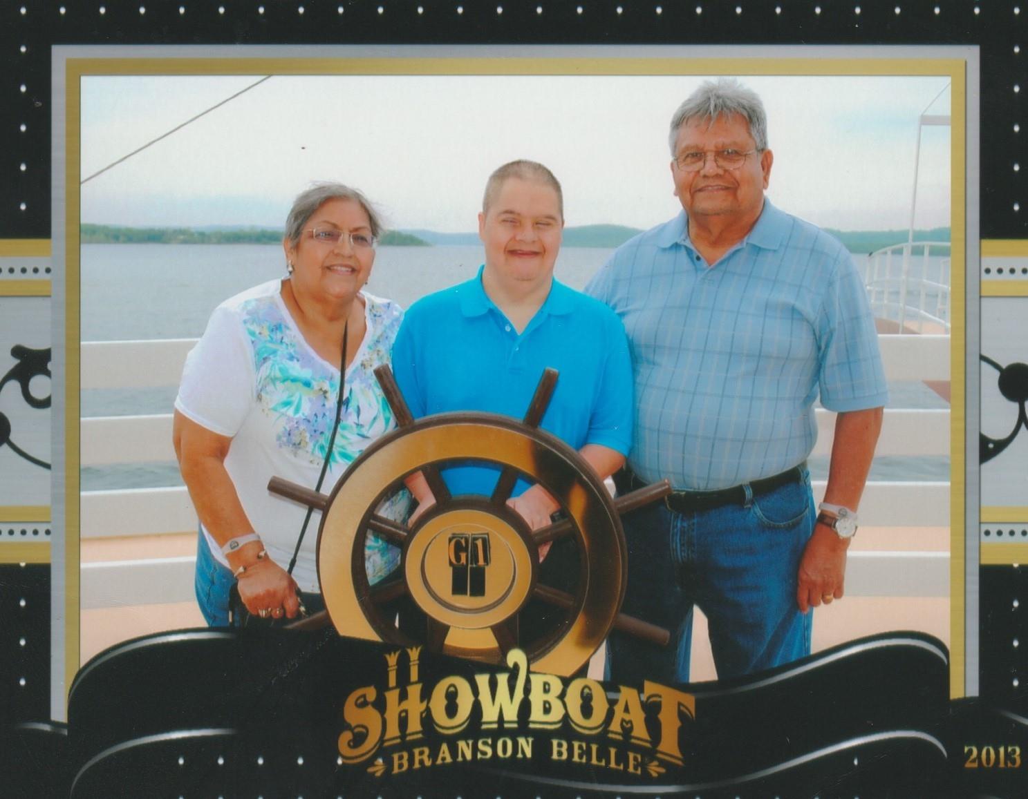 Three family members stand smiling at the boat's wheel on a sunny afternoon at the lake.