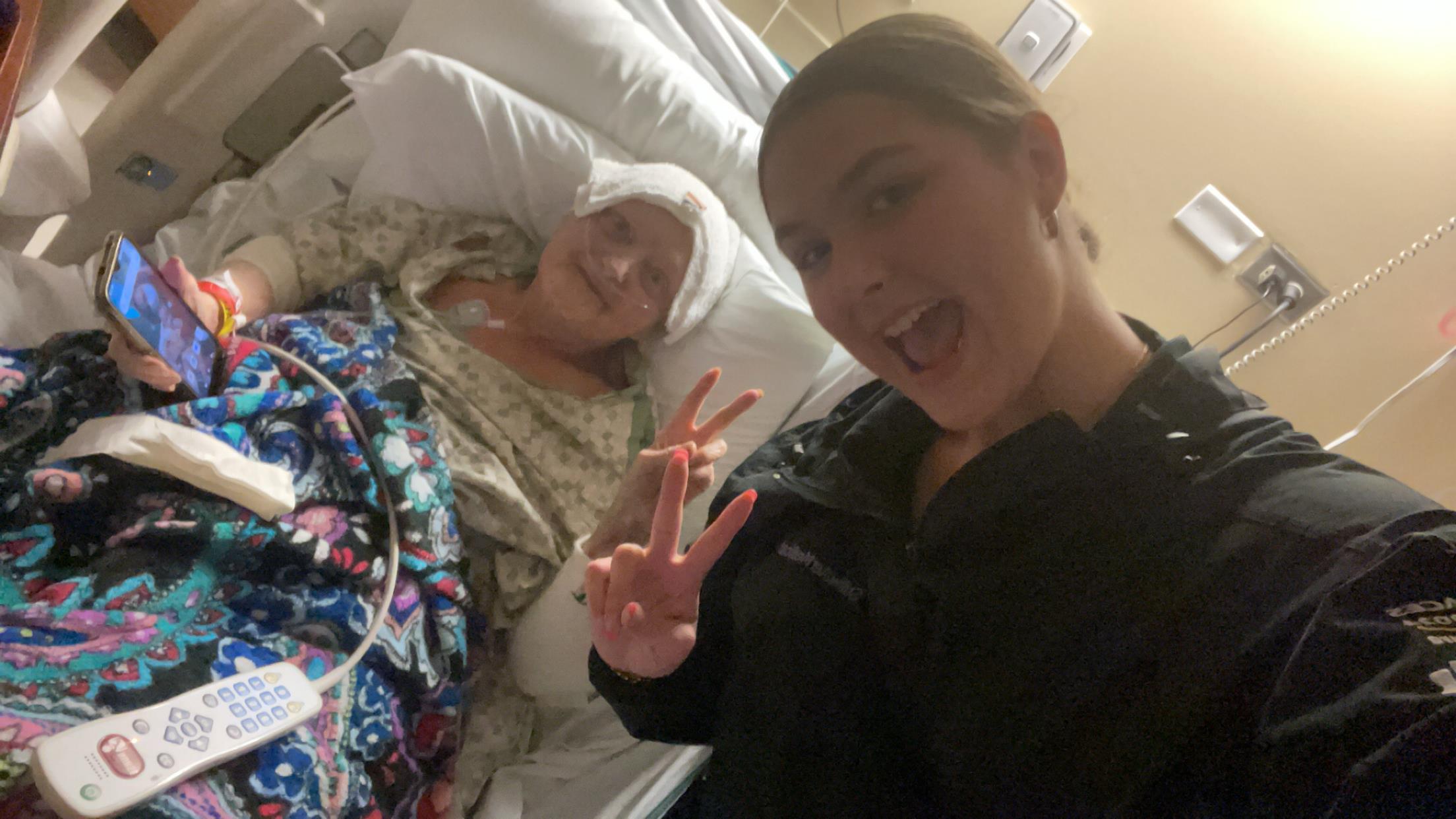 Two friends share a lighthearted moment in a hospital room, emphasizing support during recovery.