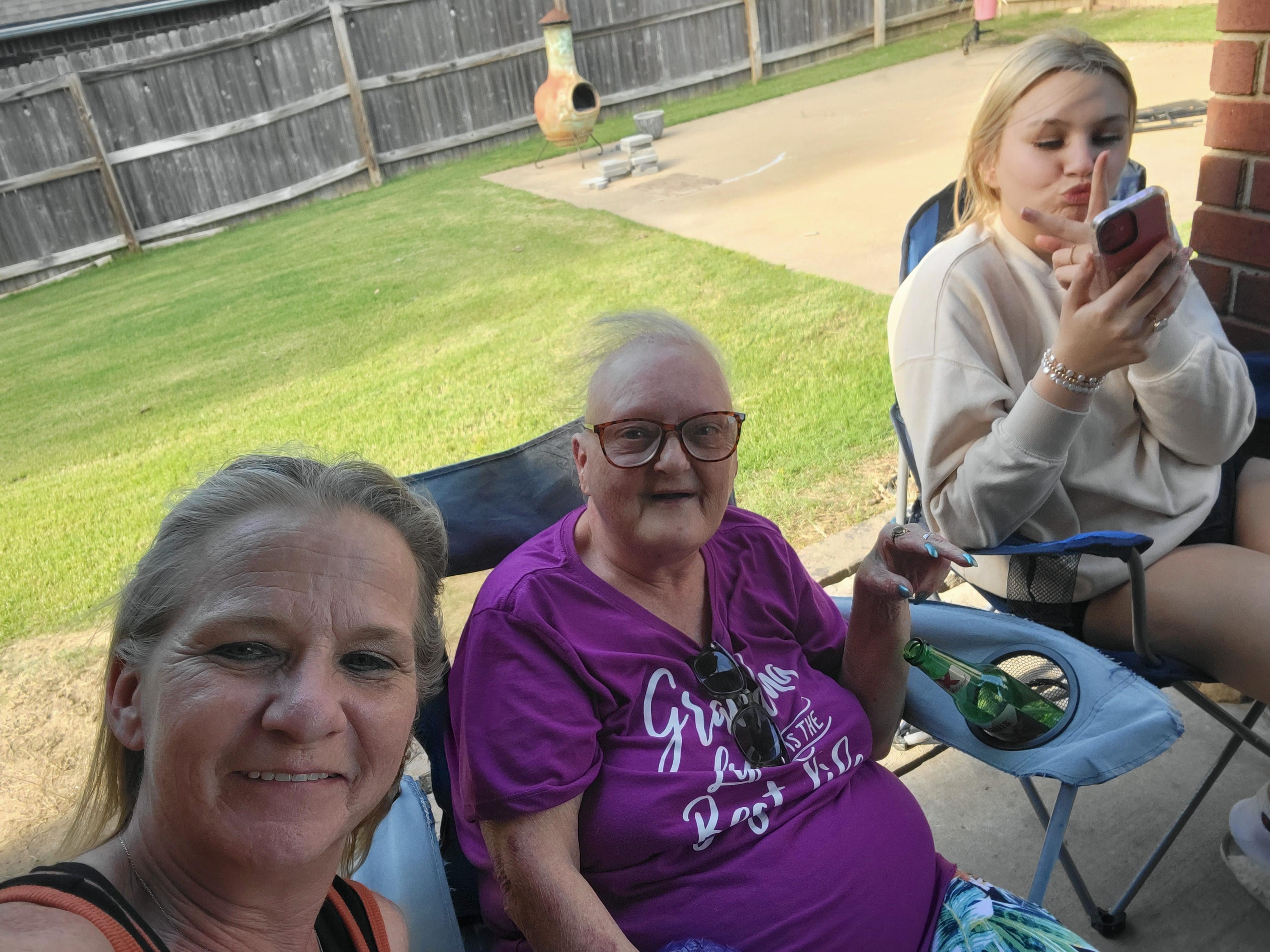 Three people enjoy a lively conversation while relaxing in chairs on a sunny day outside.
