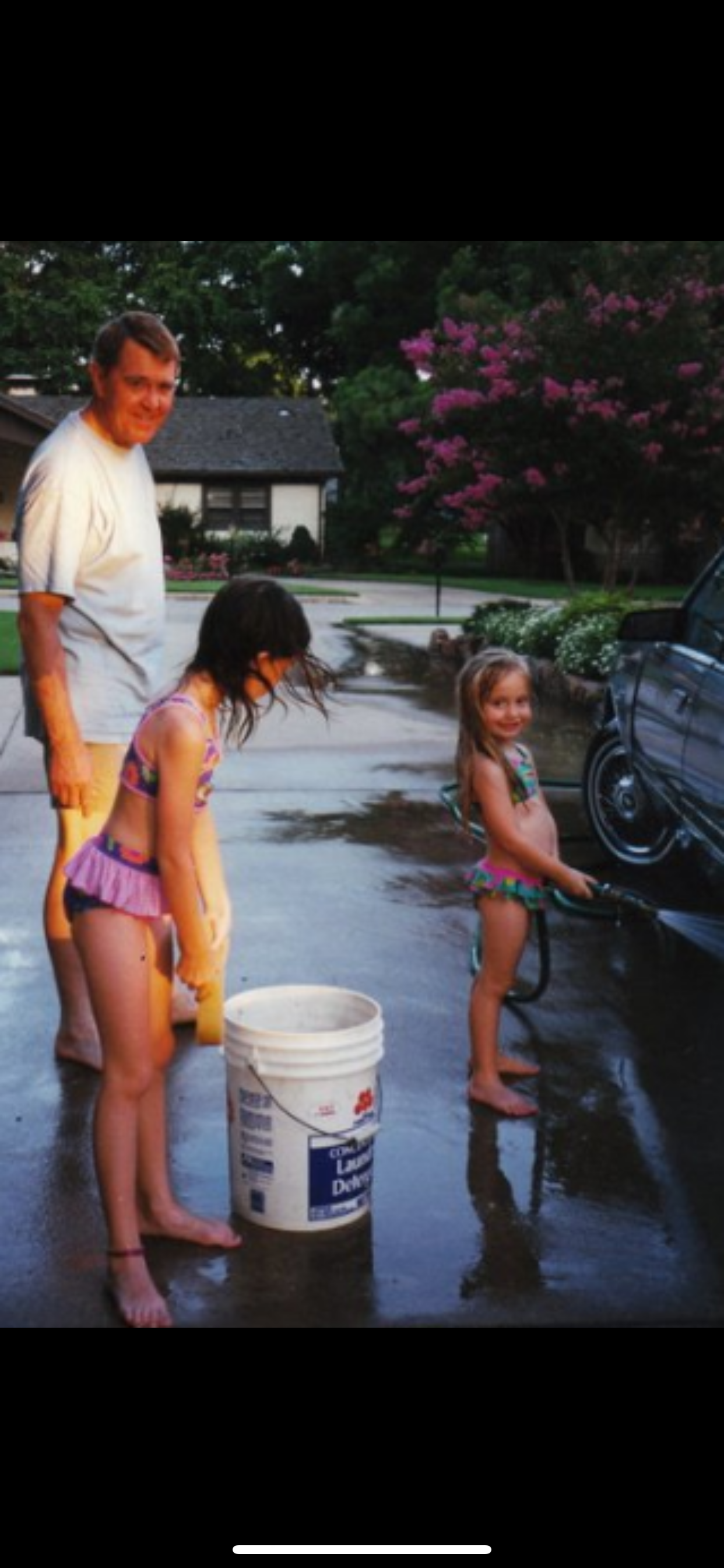 Two children and an adult engage in washing a car during a warm summer evening.
