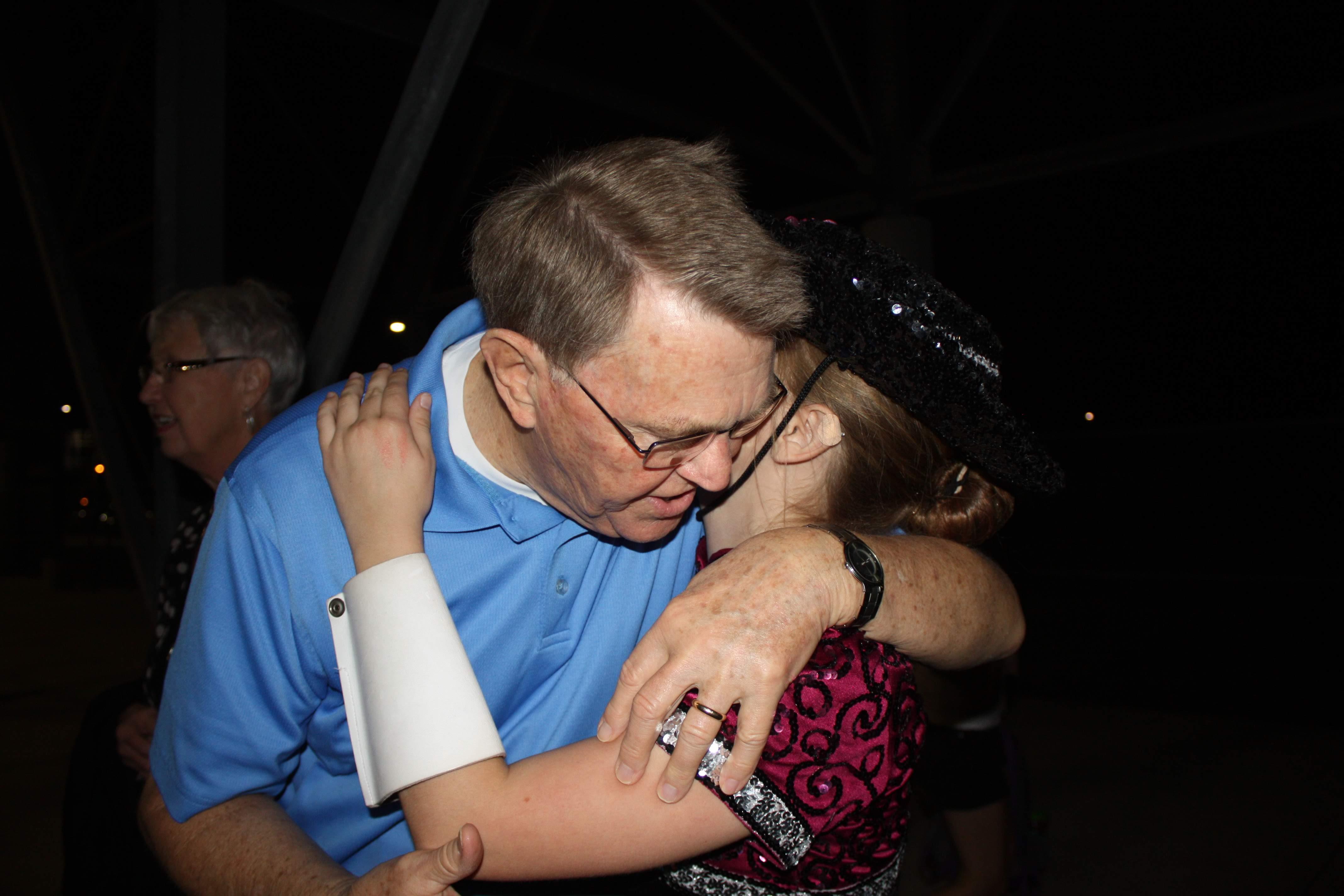 An elderly man warmly hugs a young girl, celebrating a special moment under the night sky.