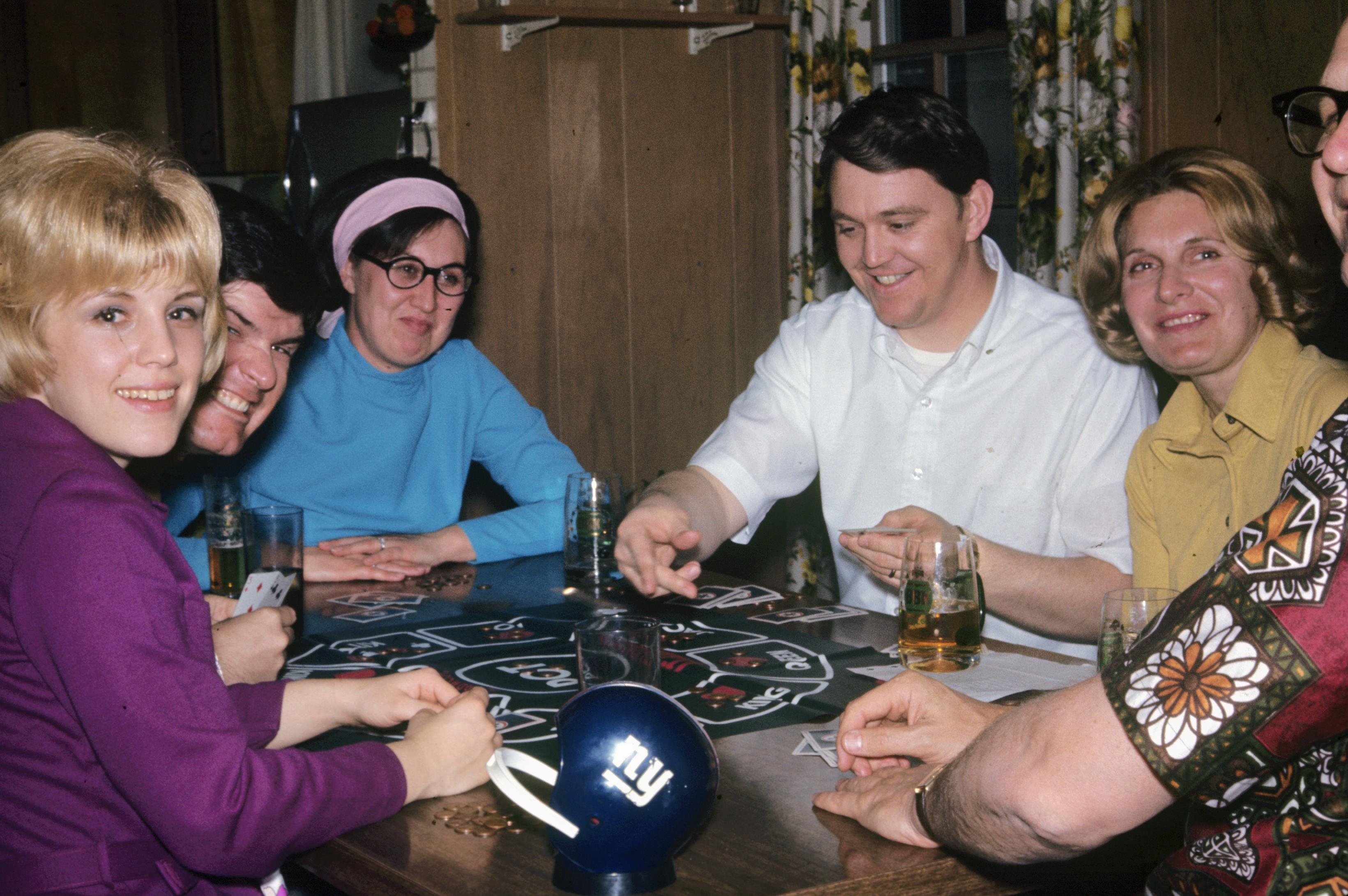 Group of friends engaged in a card game, laughing and sharing drinks in a warm atmosphere.