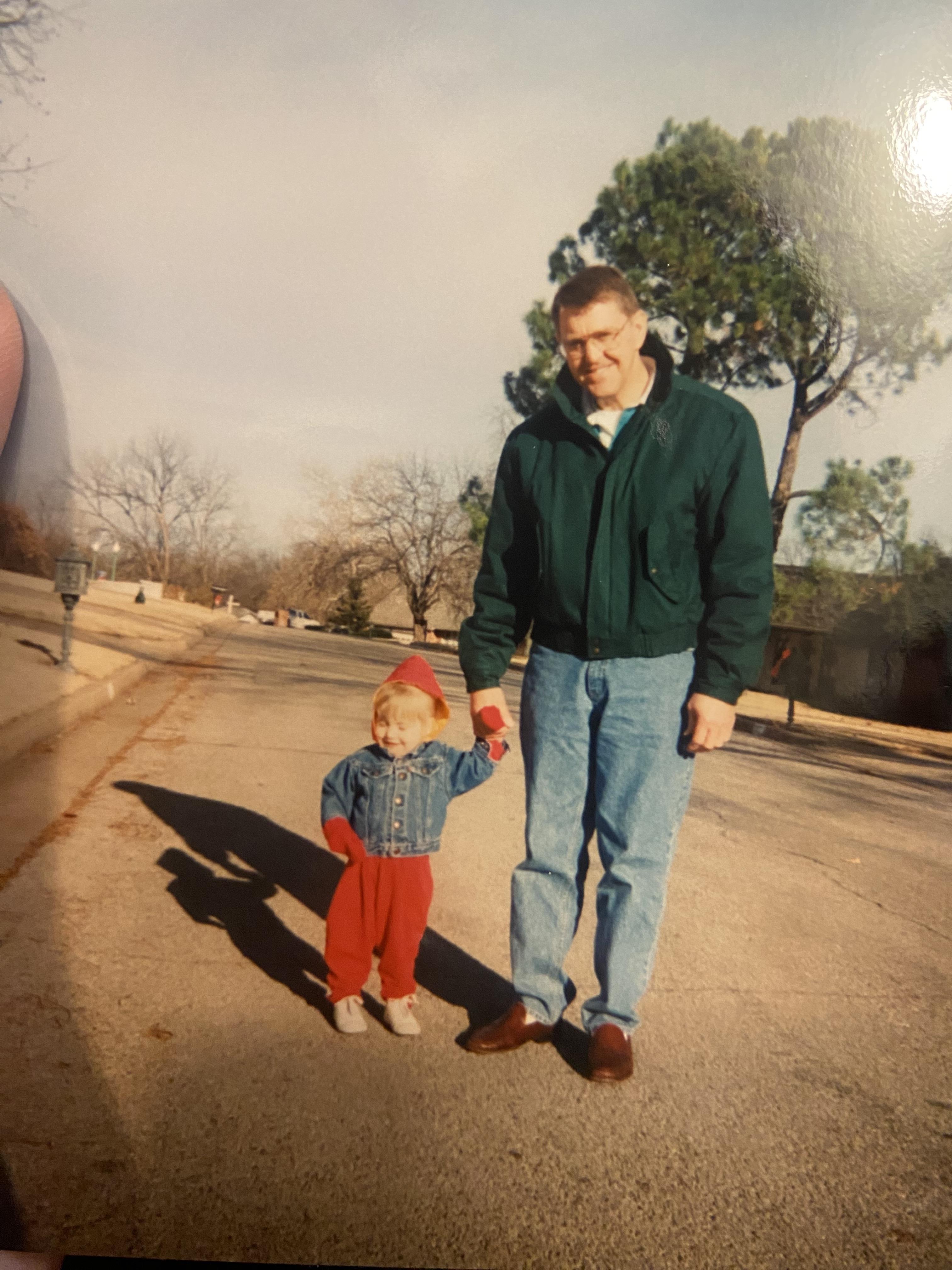 A father walks hand-in-hand with his child down a peaceful neighborhood street.