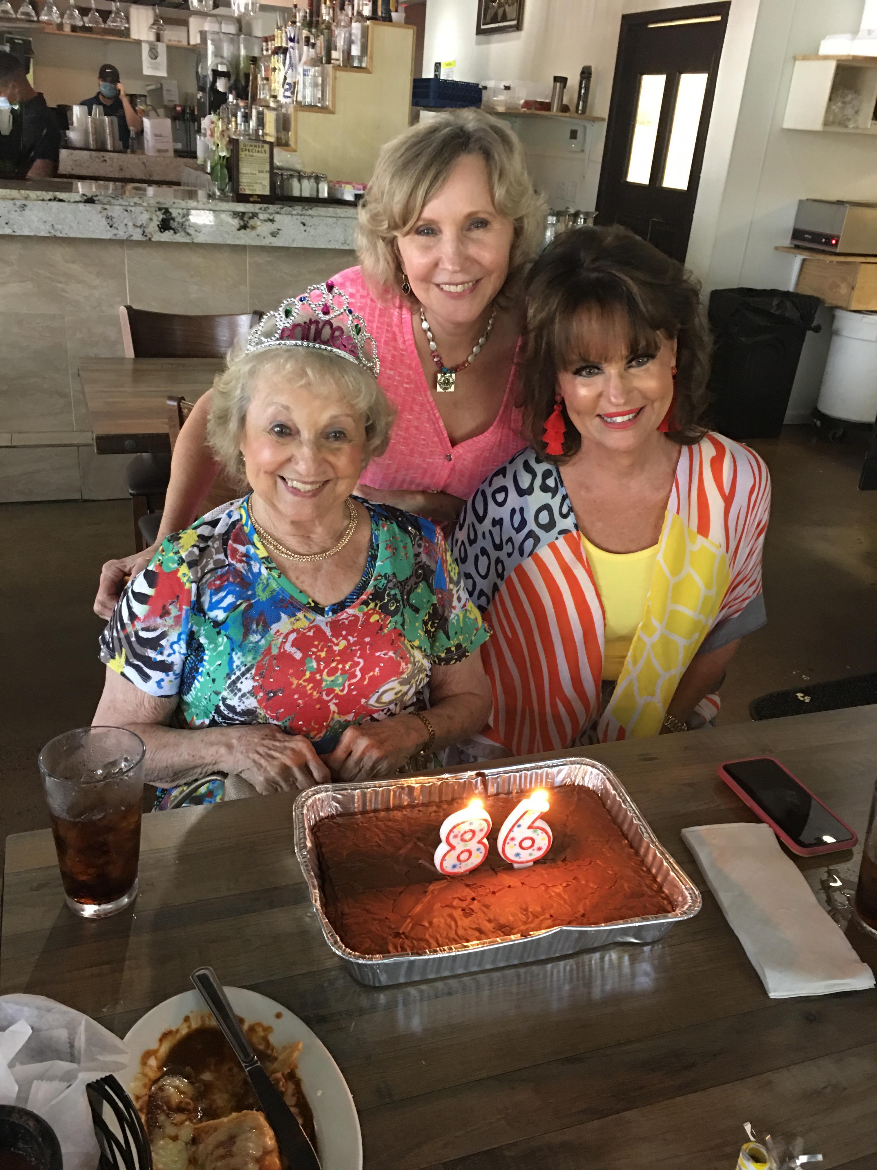 Three generations of women celebrate together, enjoying cake with candles in a vibrant restaurant.