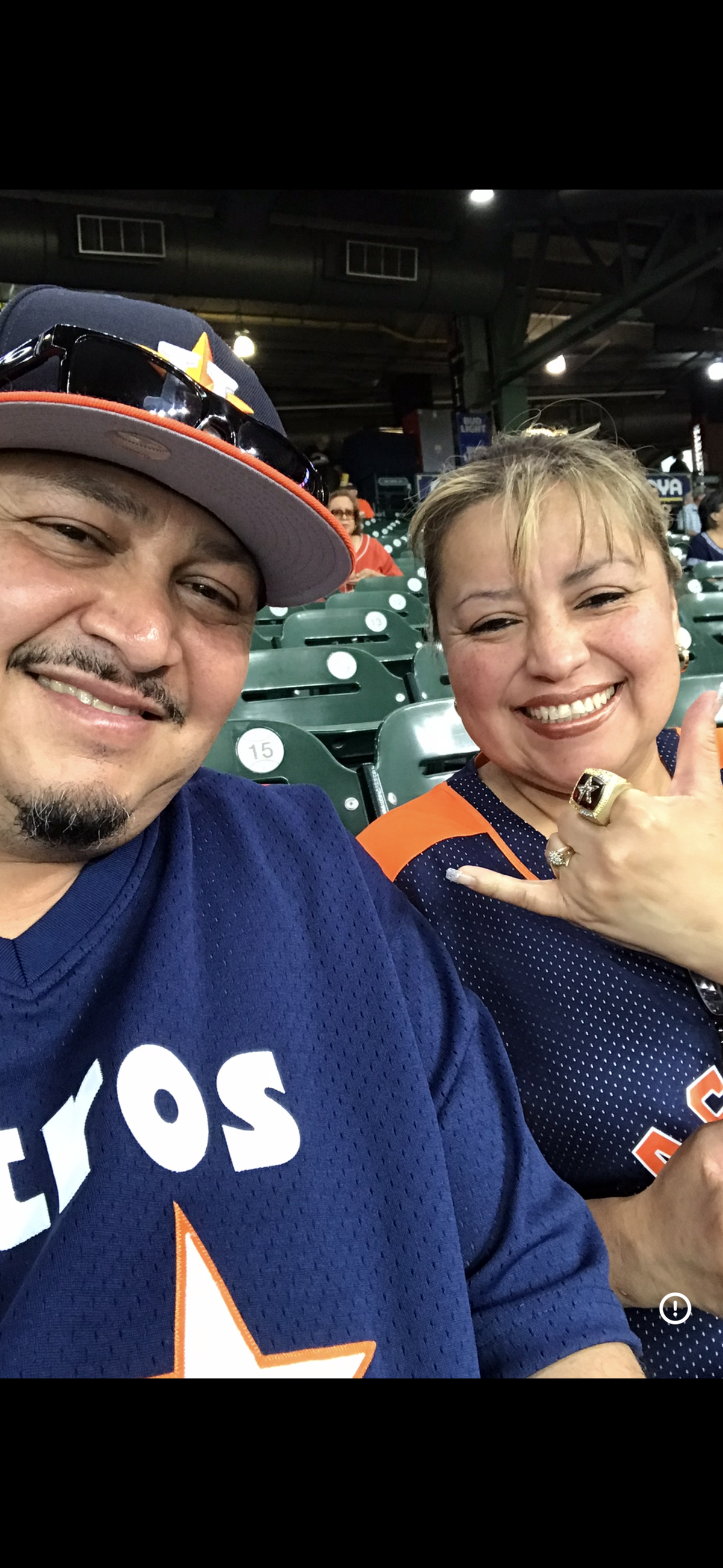 Two enthusiastic baseball fans smile while sitting in the stands at a game.