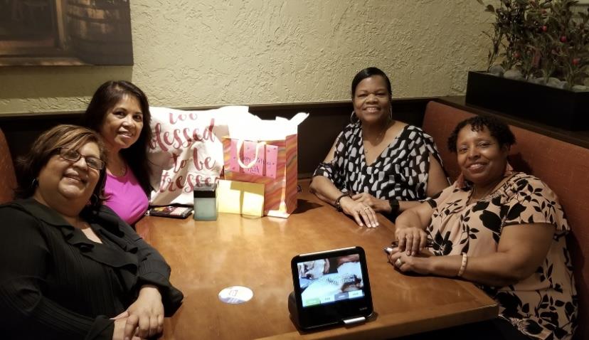 Four friends share smiles and gifts at a lively restaurant table.