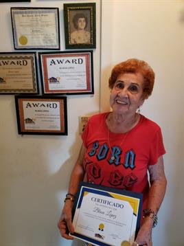 A senior woman smiles while holding a certificate in her living room, showcasing her achievements.
