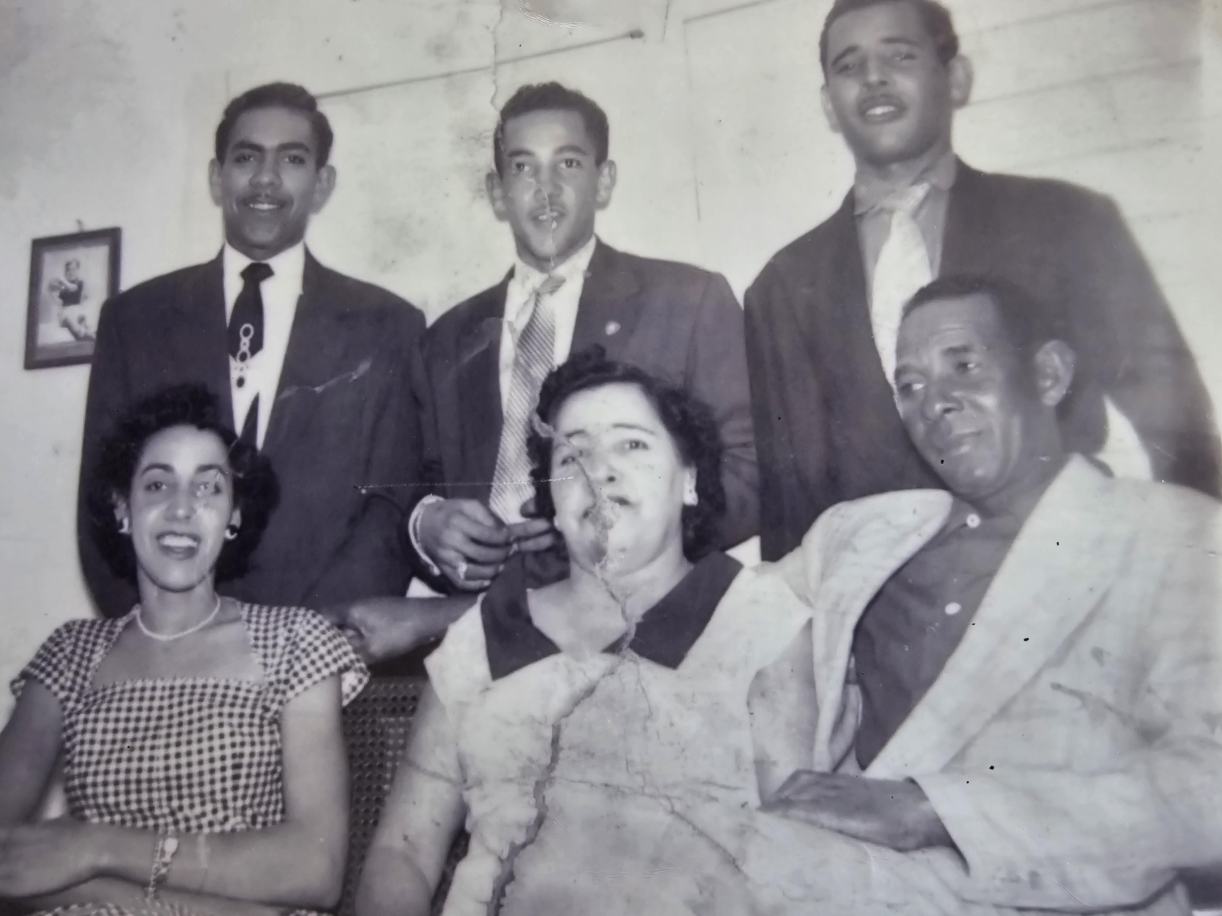Group of six people smiling and posing together in a nostalgic indoor setting from the past.
