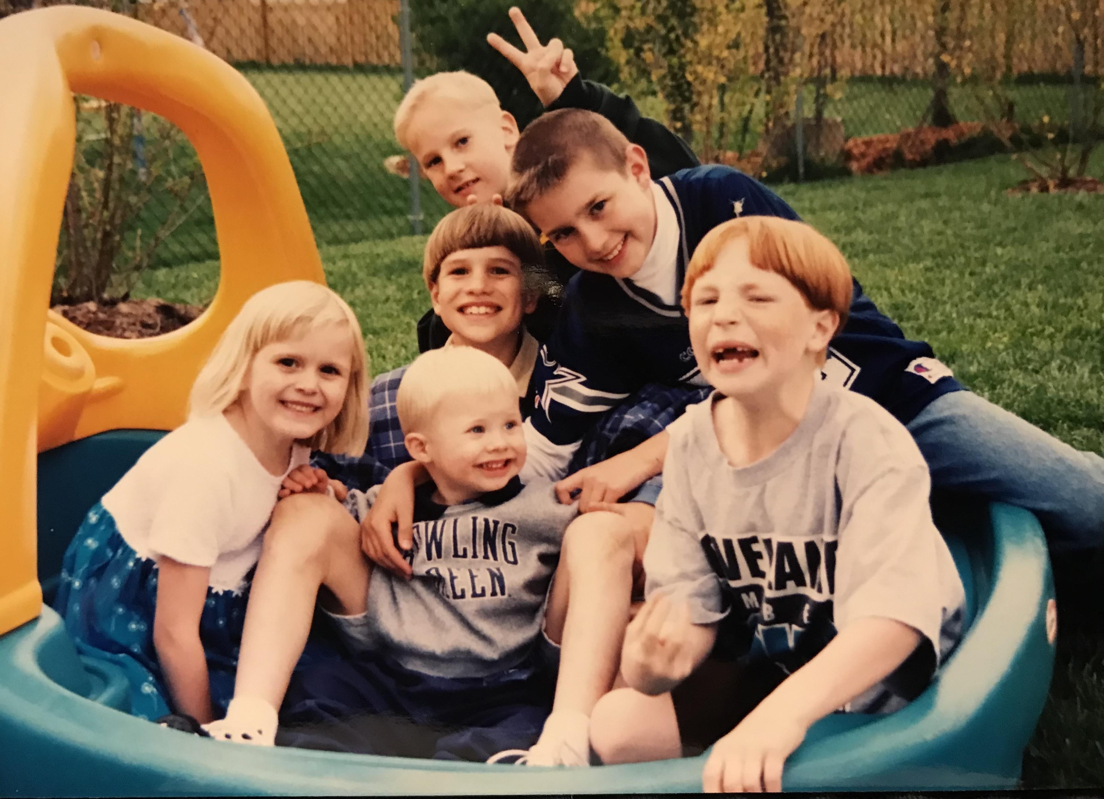 A group of six children joyfully playing in a sandbox and slide on a bright day.