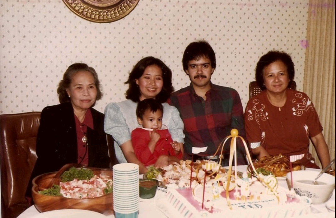 Five family members gather around a table filled with traditional dishes and a decorated cake.