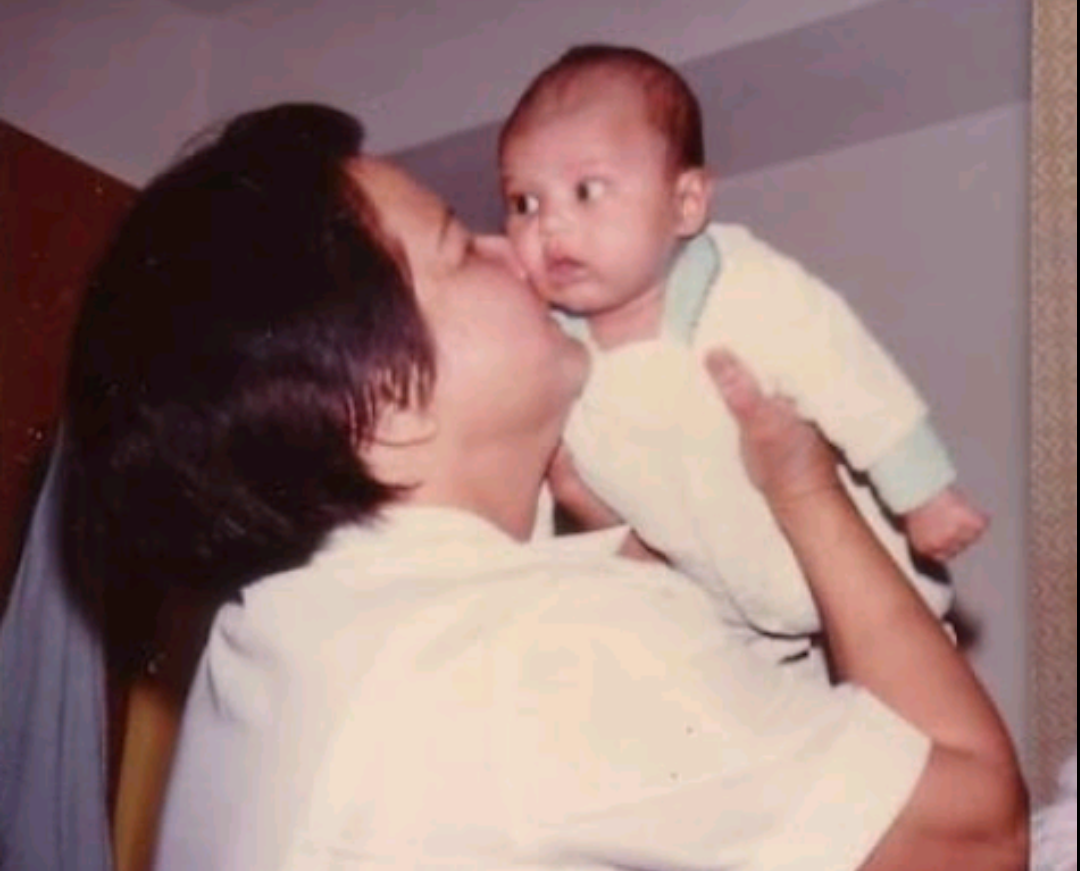 A father shows affection by kissing his baby while gently holding them indoors.