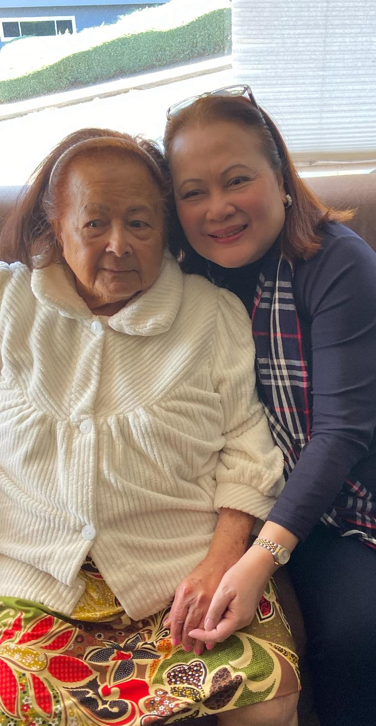 An elderly woman smiles with her companion, sharing a heartfelt moment indoors.