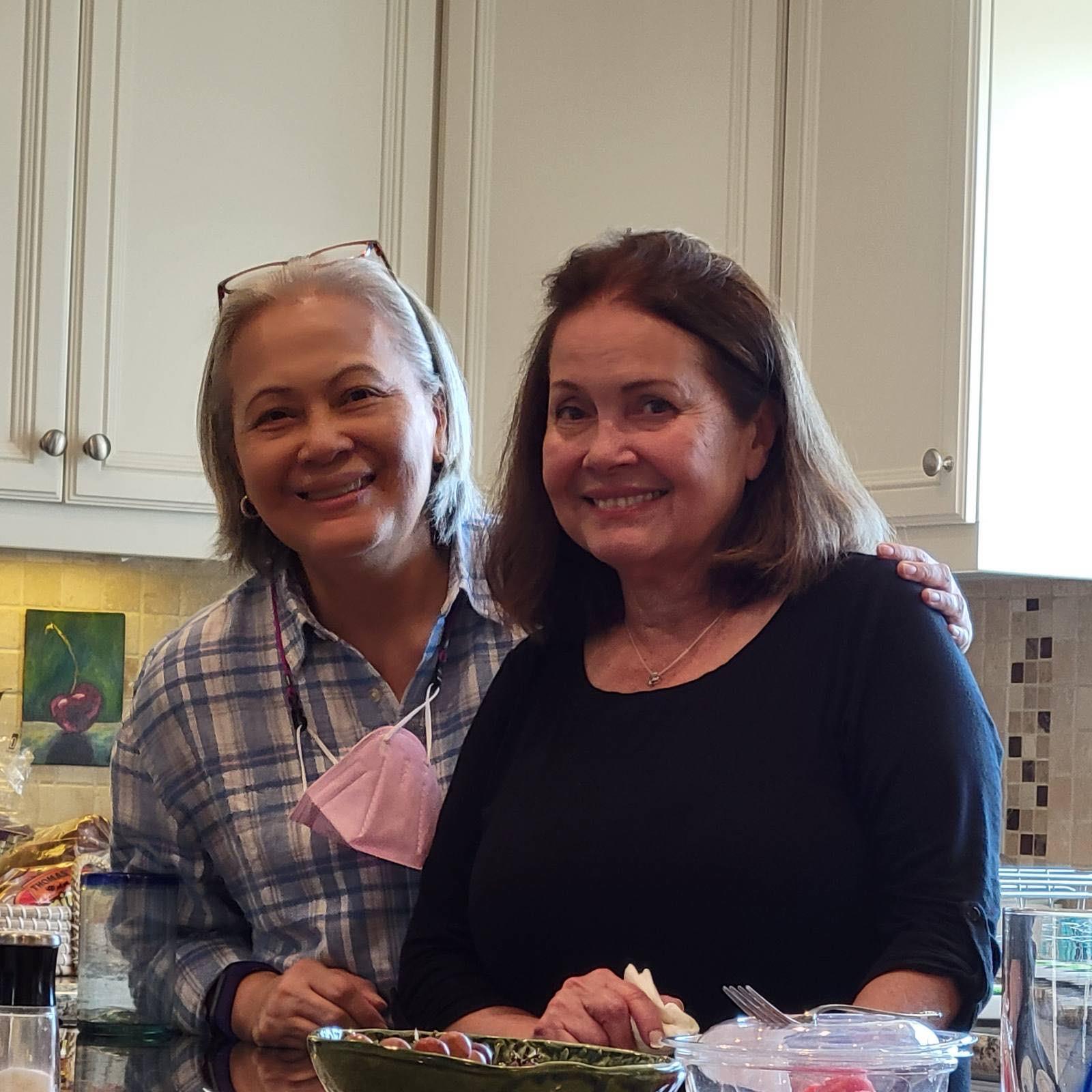 Two friends smile while preparing food in a bright, well-equipped kitchen.