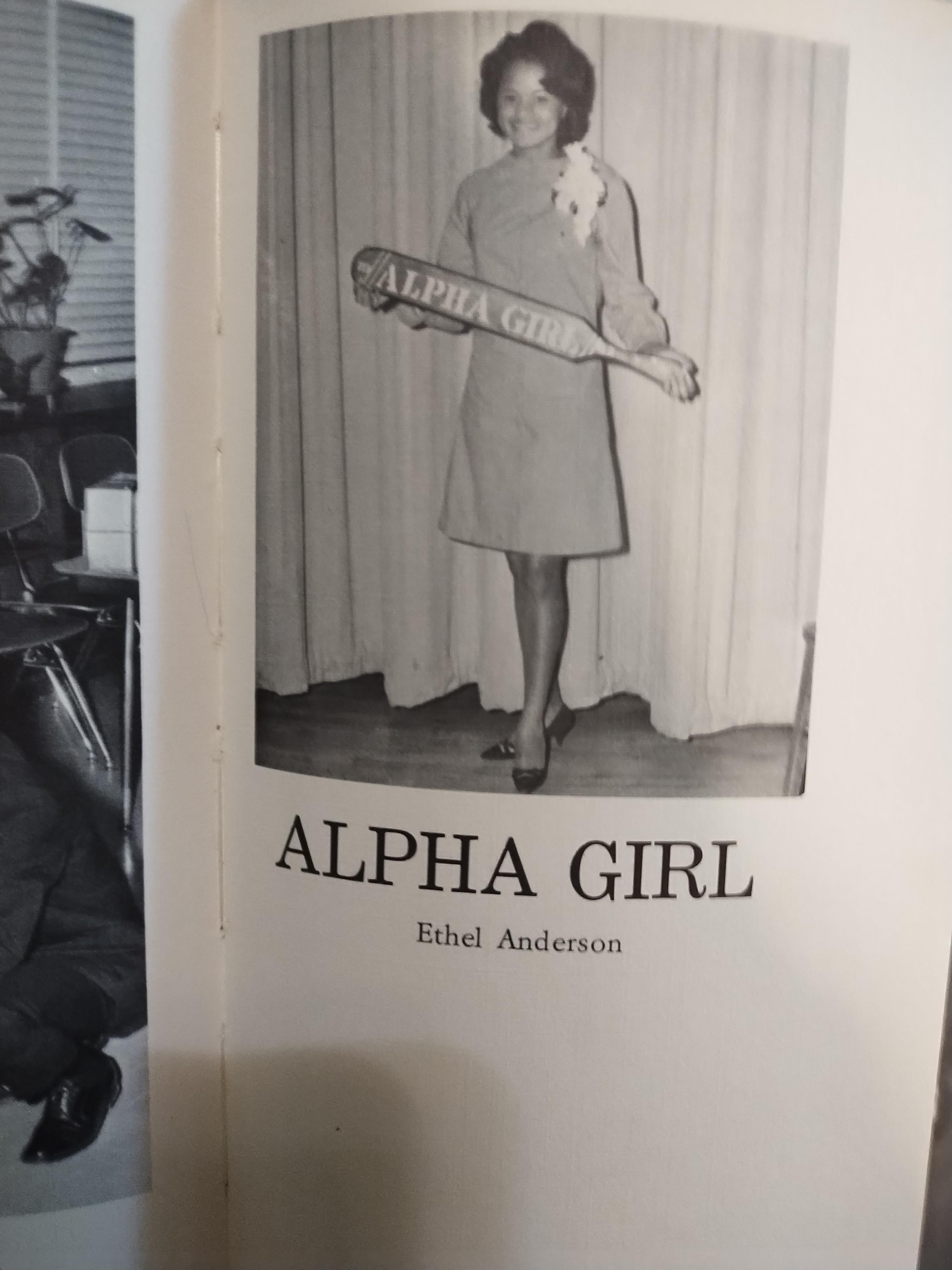 Ethel Anderson stands confidently in a dress while holding a sign that says Alpha Girl.