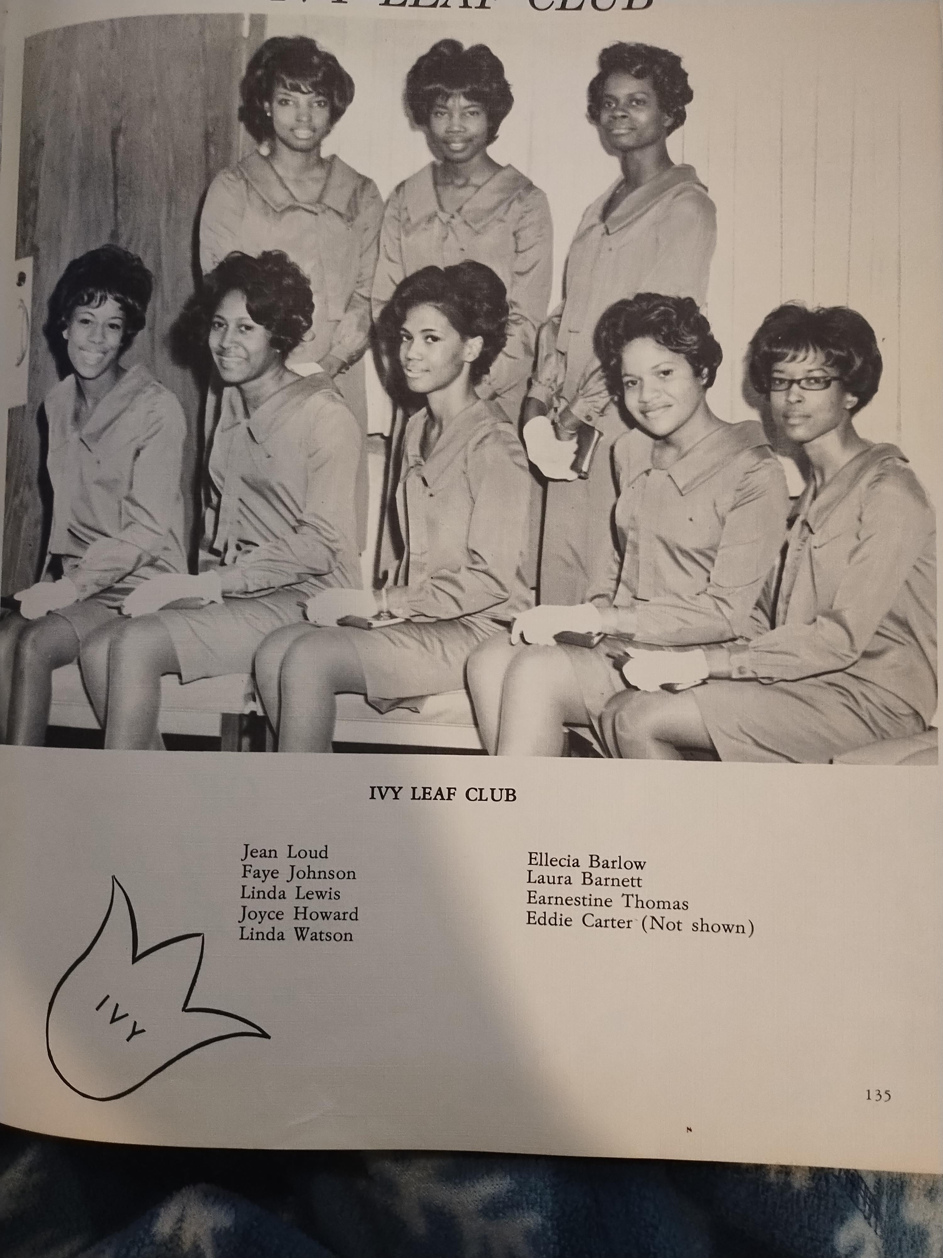 A group of seven women dressed in matching outfits gather for a formal photo at an event.
