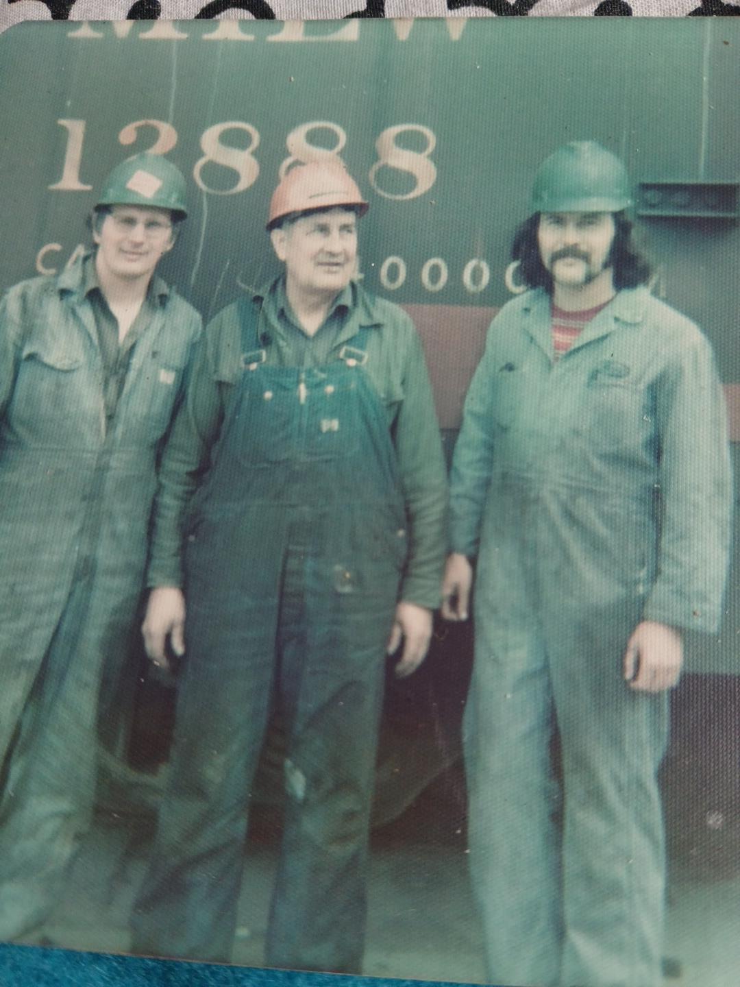 Three workers in overalls and hard hats demonstrate teamwork and dedication.