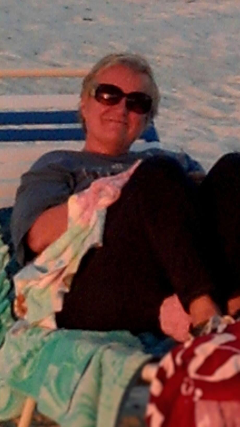 A woman enjoys her time on the sandy beach at sunset, wrapped in a cozy blanket.