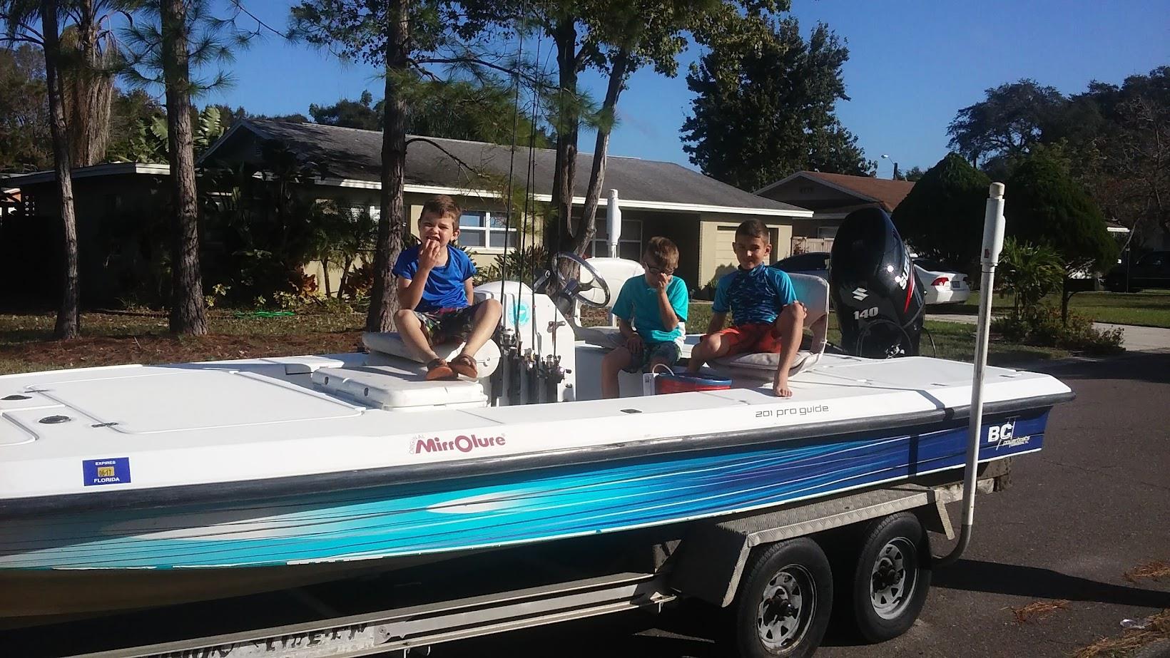 Three people relax on a boat parked on a trailer outside a house, ready for a fun day on the water.