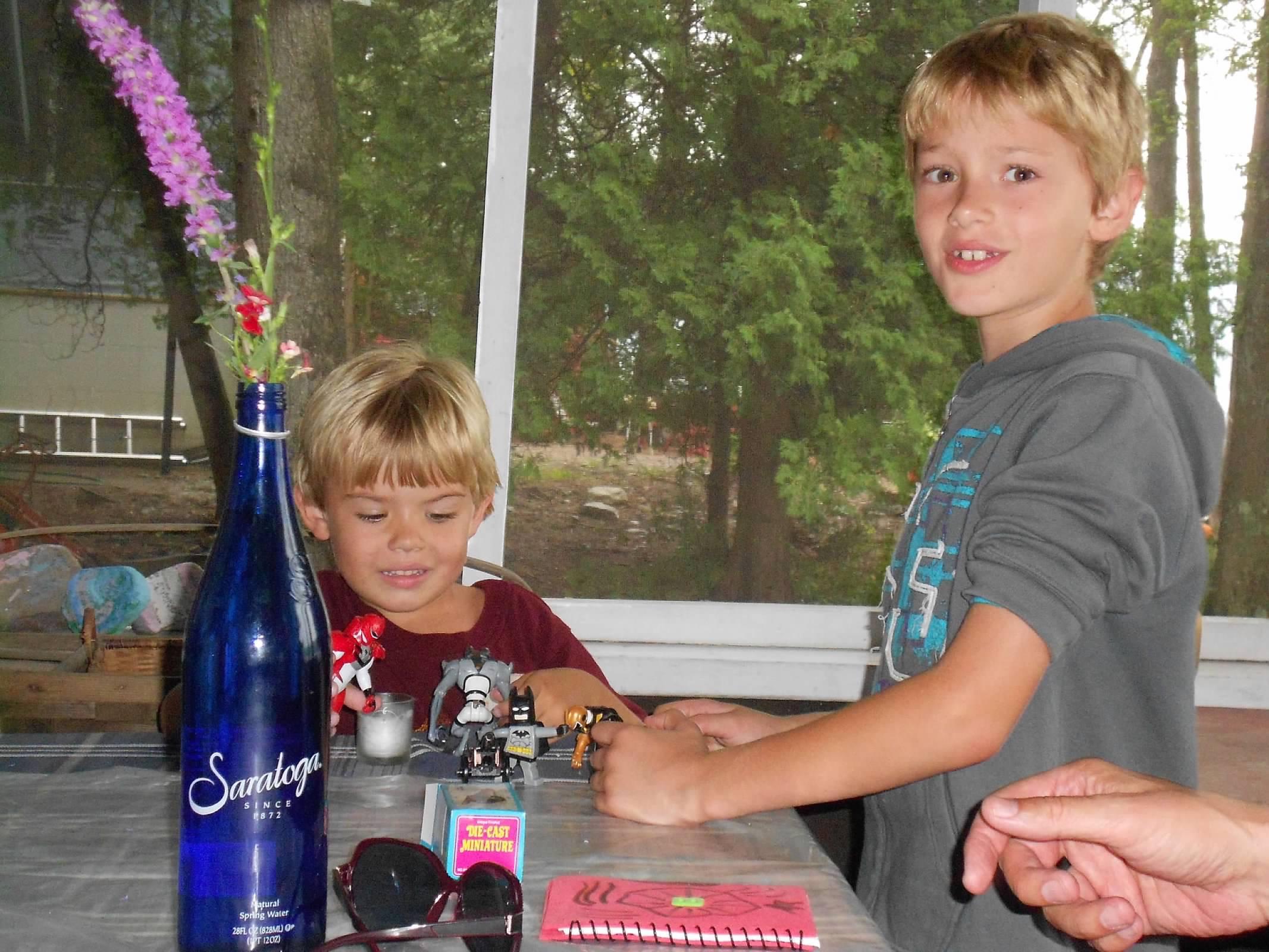 Two boys engaged in playtime with action figures on a table inside a screen porch.