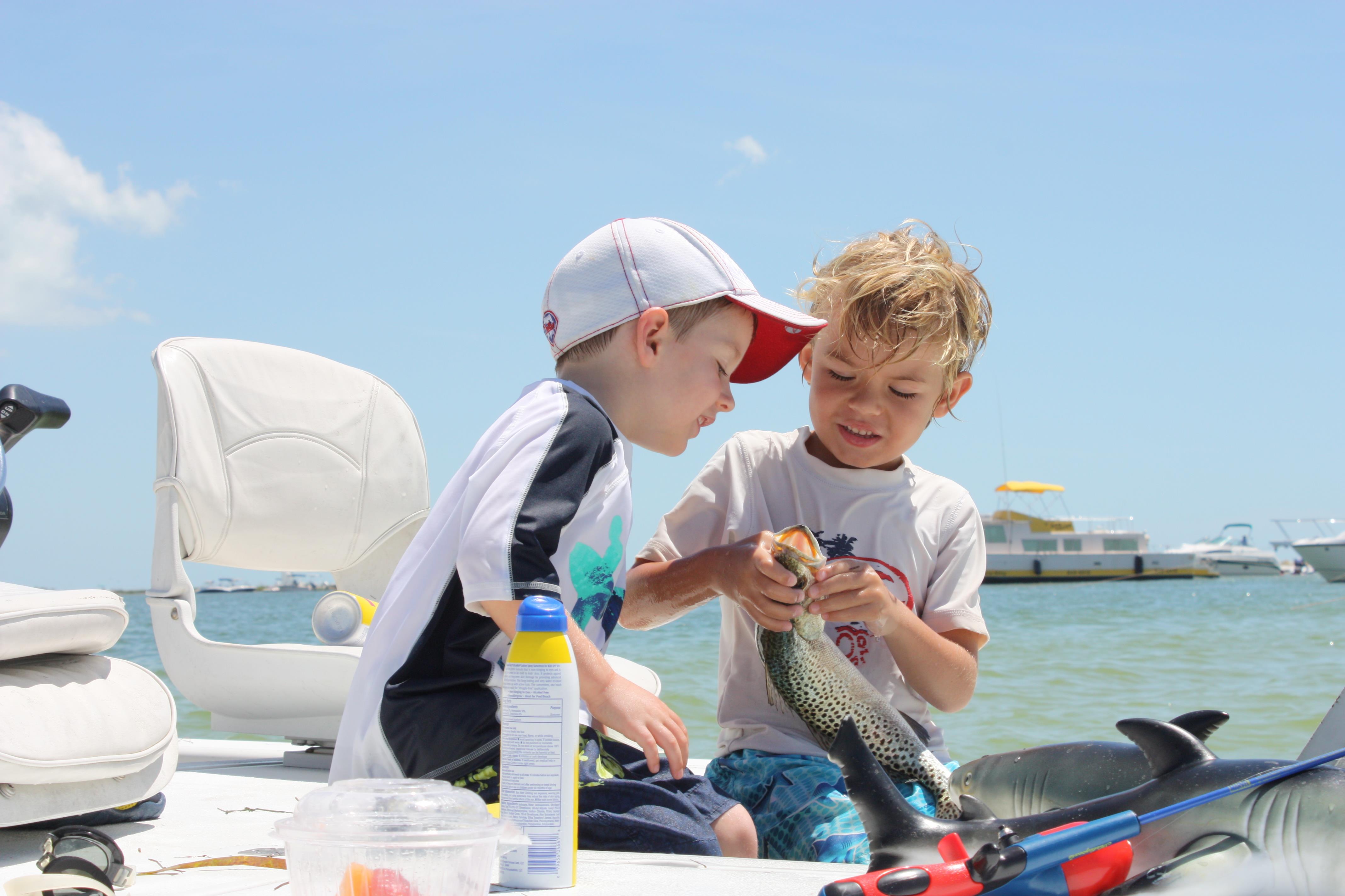 Boys enjoy fishing on a boat, excitedly holding a freshly caught fish under a clear blue sky.
