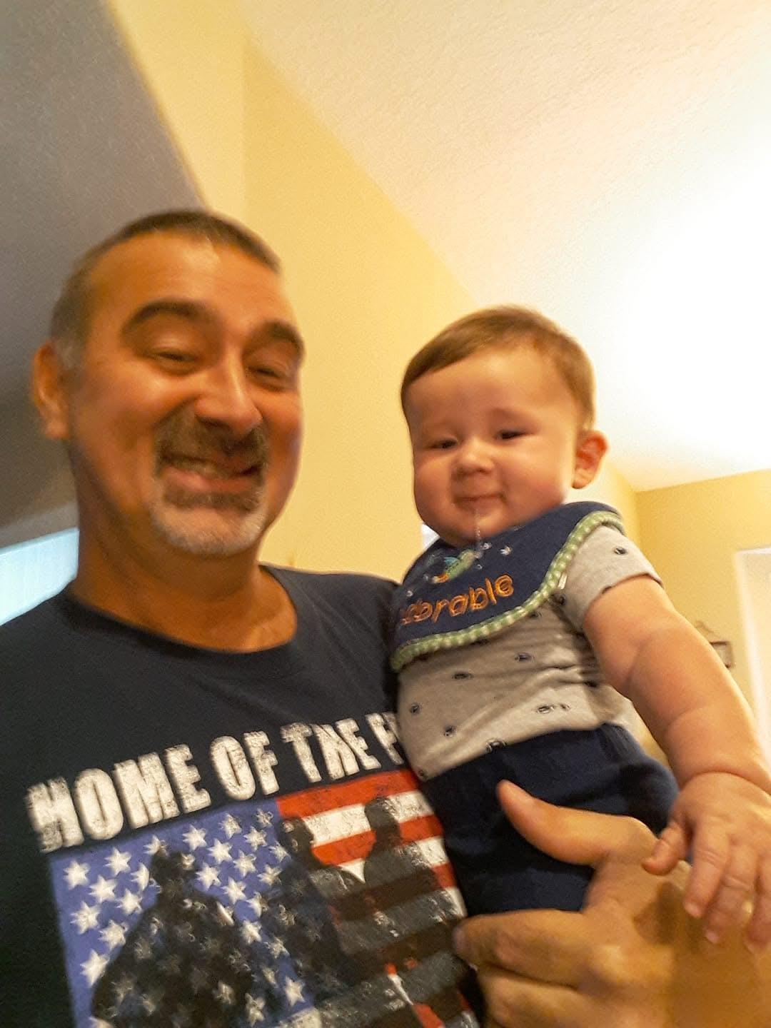 A smiling grandparent holds a happy baby in a cozy indoor setting, sharing a joyful moment together.