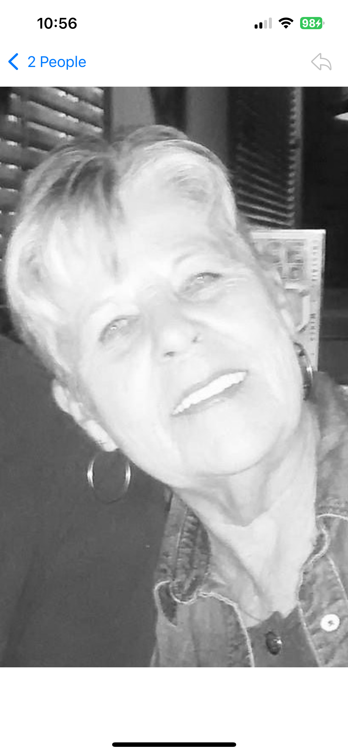 An older woman with short hair and earrings beams with joy while enjoying time with others.