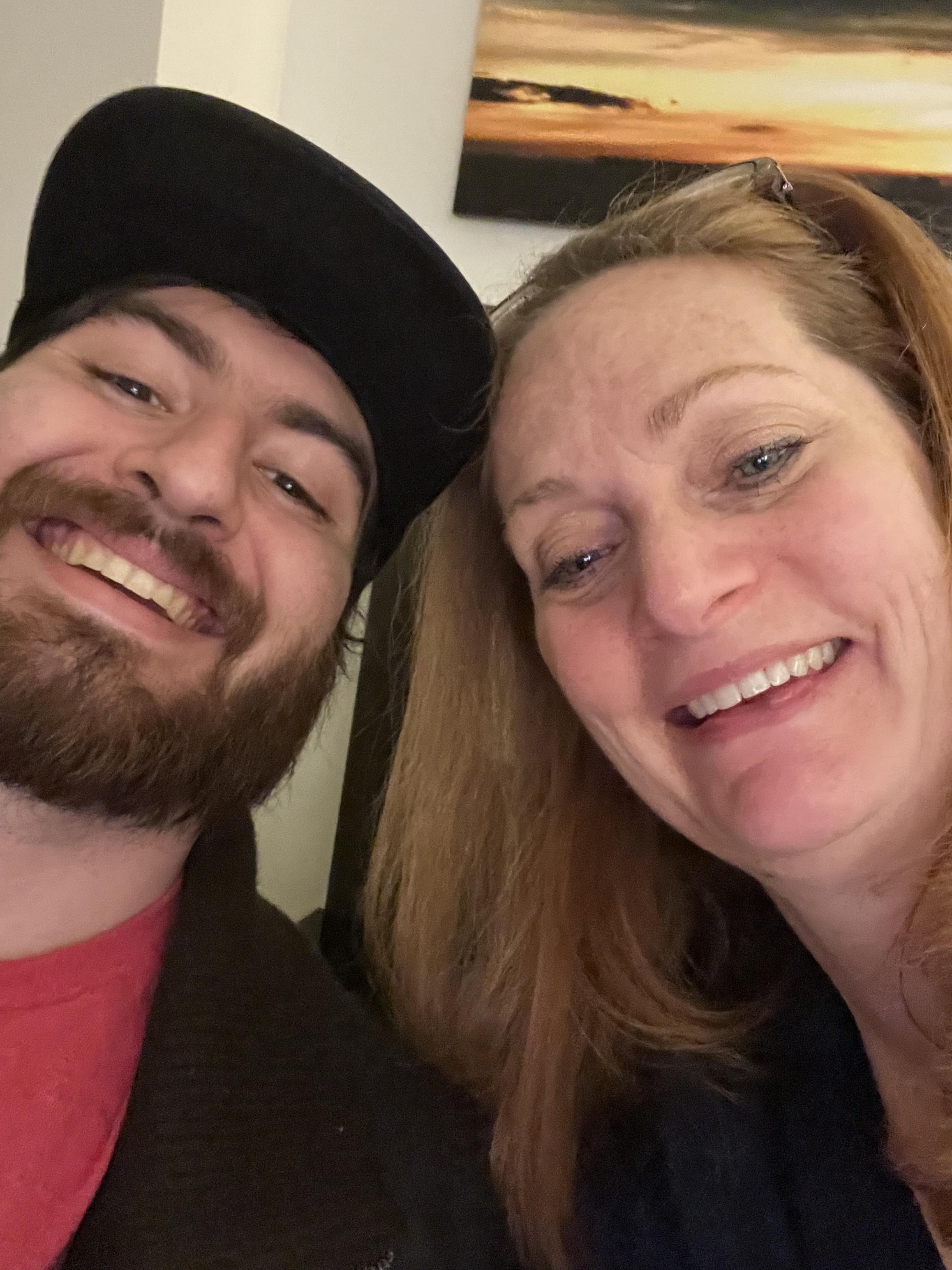 Two friends smile widely for a selfie, enjoying their time together in a comfortable atmosphere.