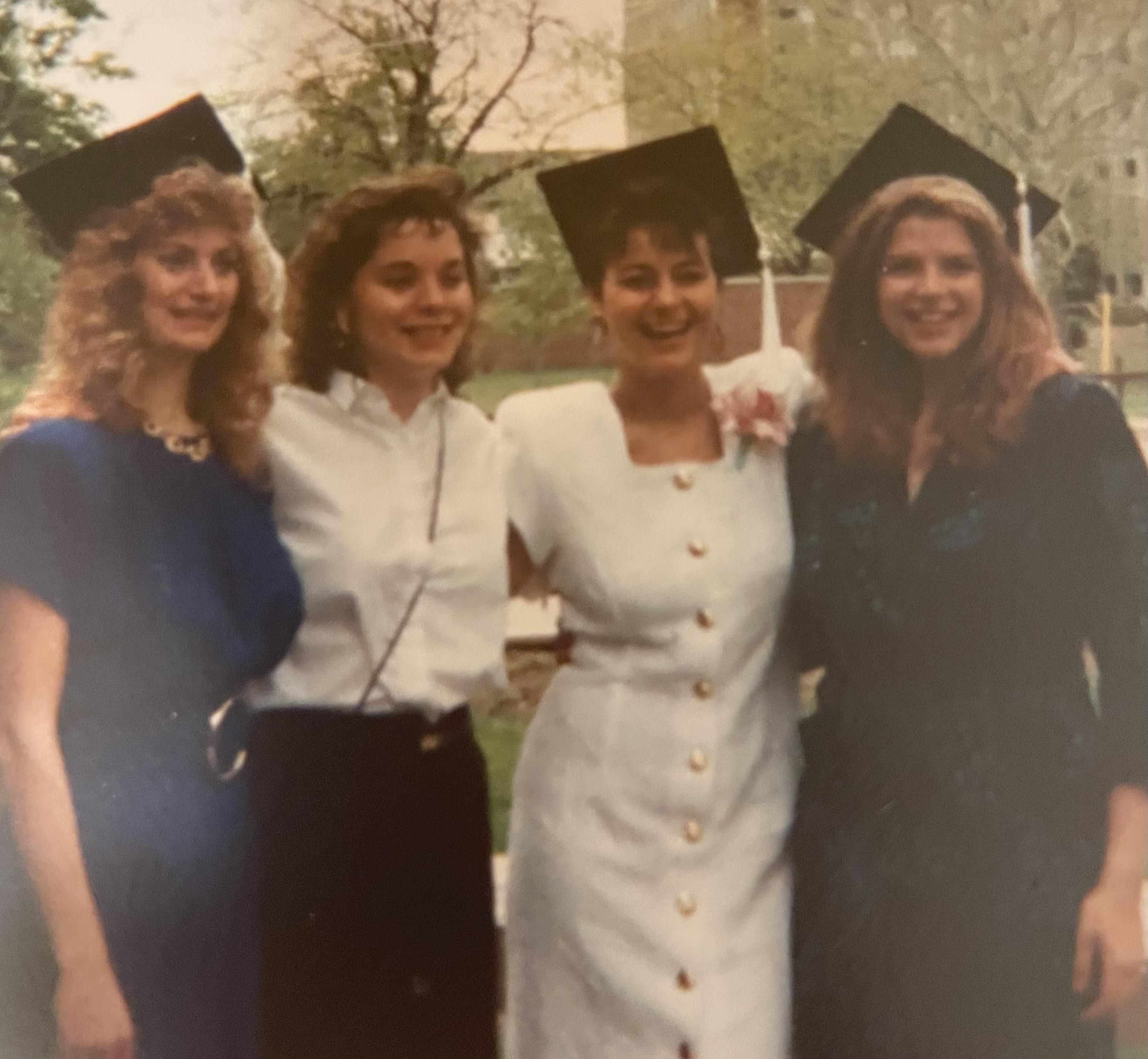 Four friends proudly pose in graduation caps while celebrating their achievement outdoors.