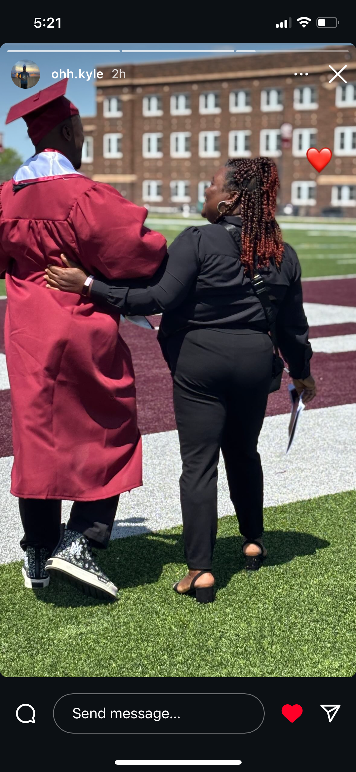 A graduate in a red gown shares a heartwarming moment with a family member on the field.
