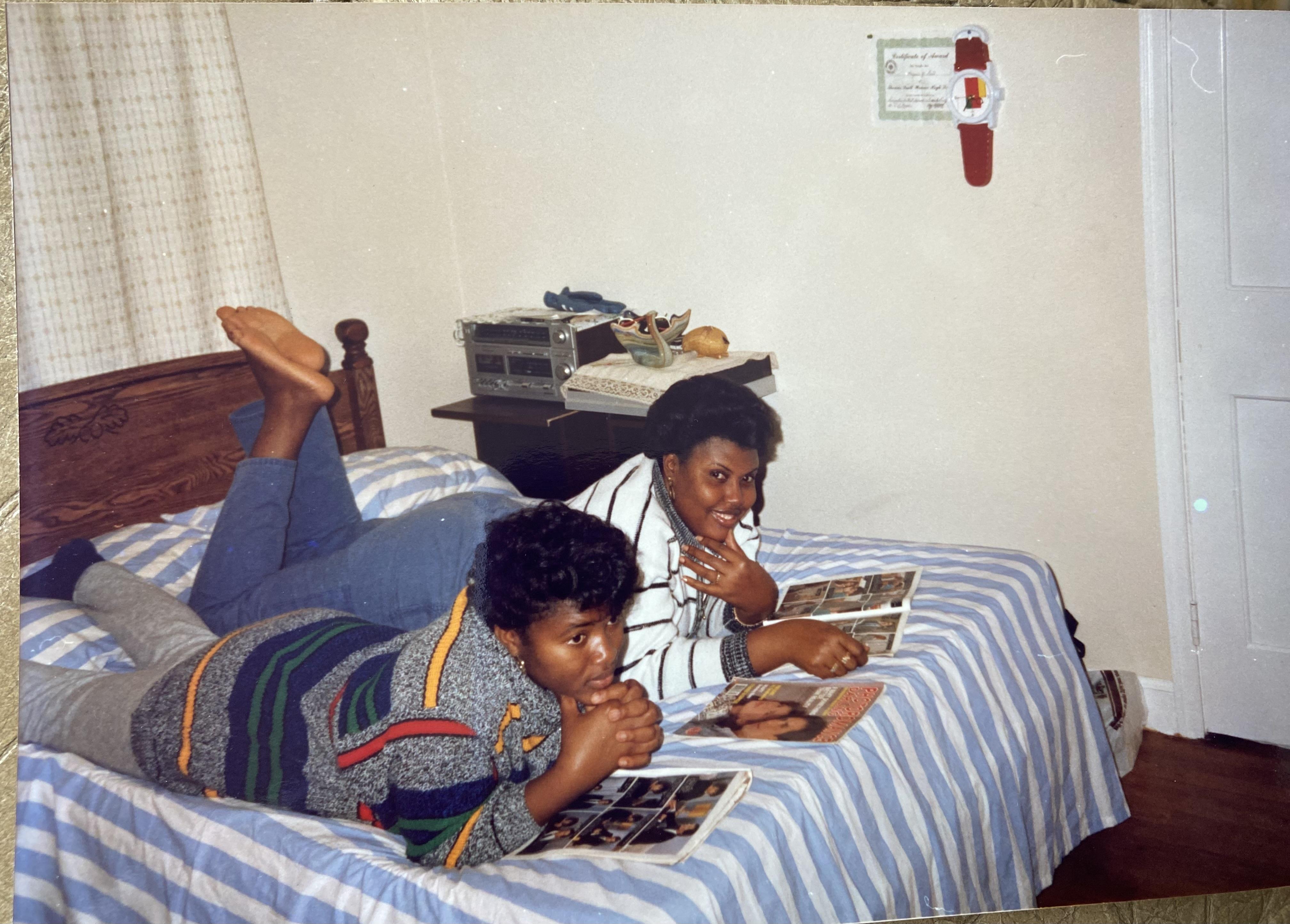 Two friends relax on a bed while browsing magazines, enjoying each other's company indoors.