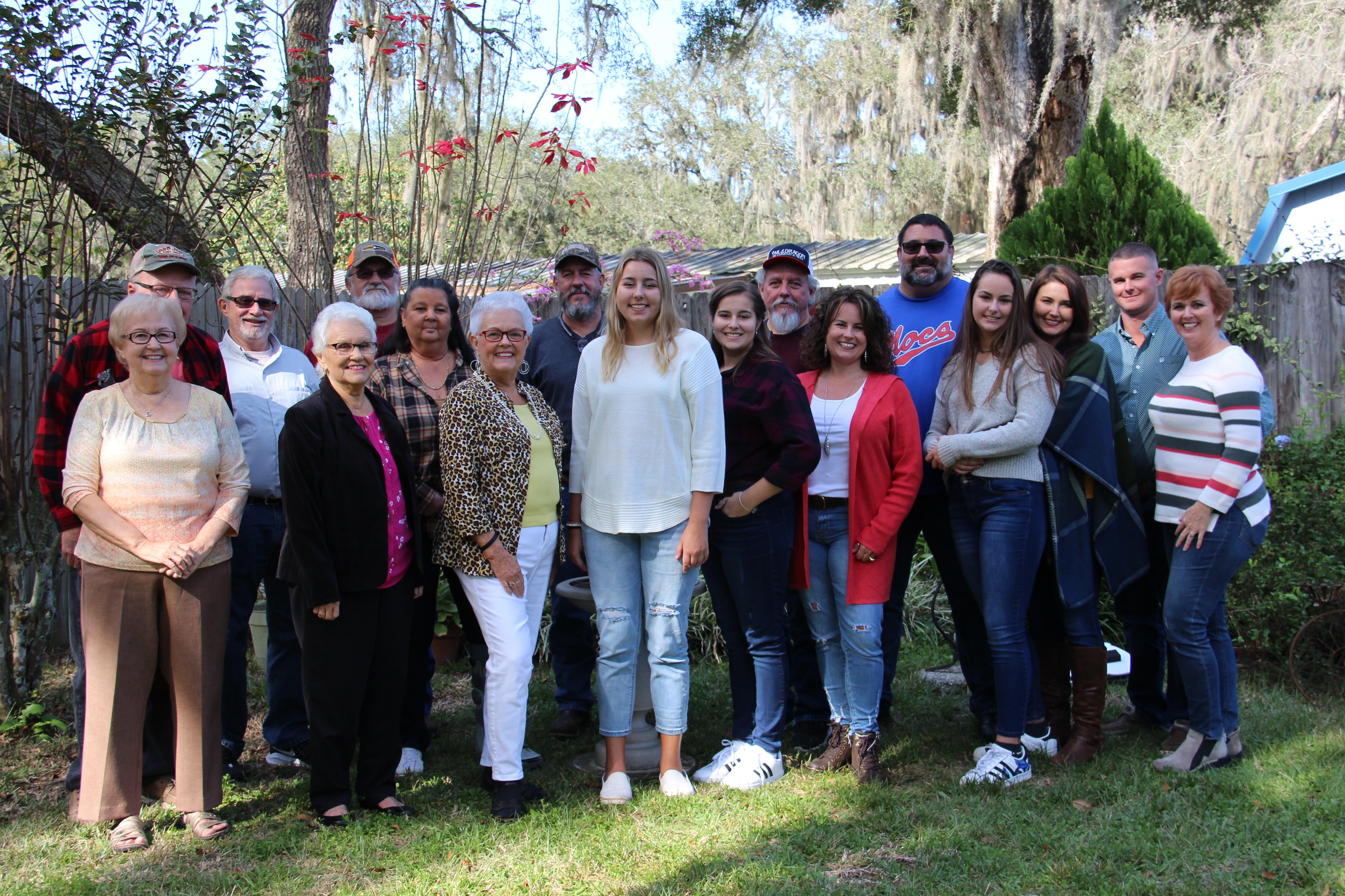 Group of family members smiling and posing together in a grassy backyard setting on a sunny day.