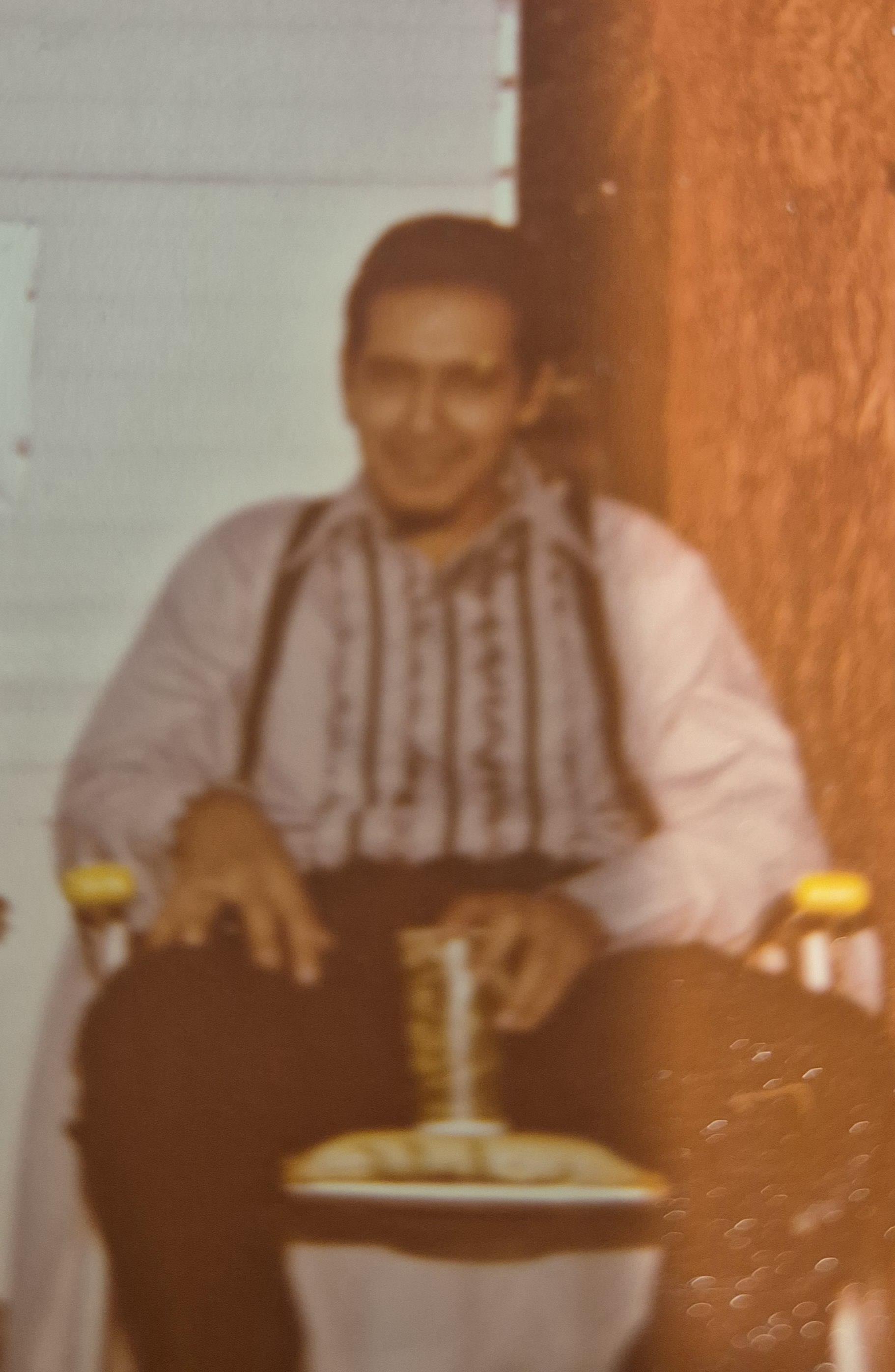 Man in traditional clothing relaxes on a porch during the afternoon, holding a drink.