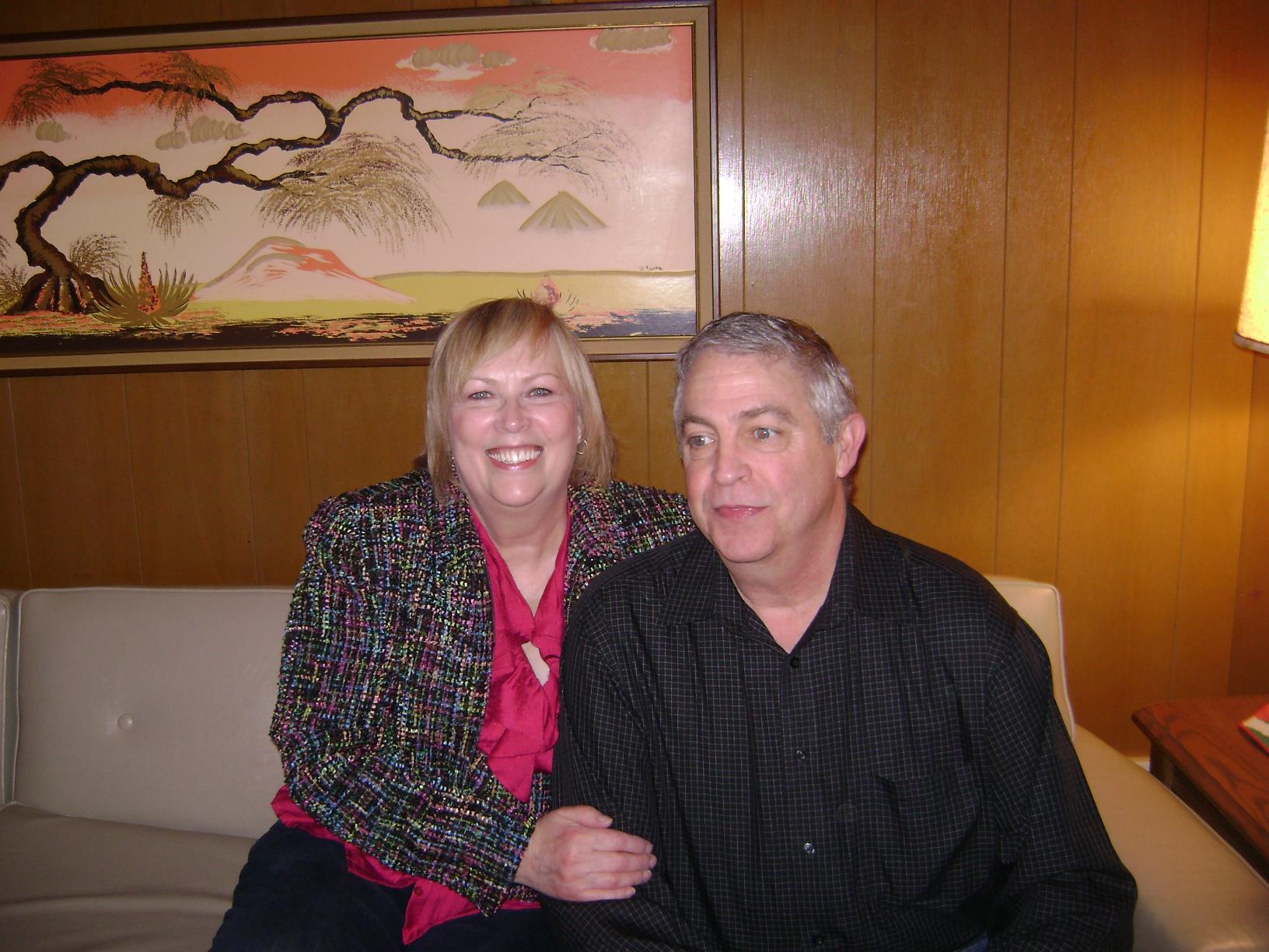 A couple enjoys each other's company in a warmly lit room with vintage decor behind them.