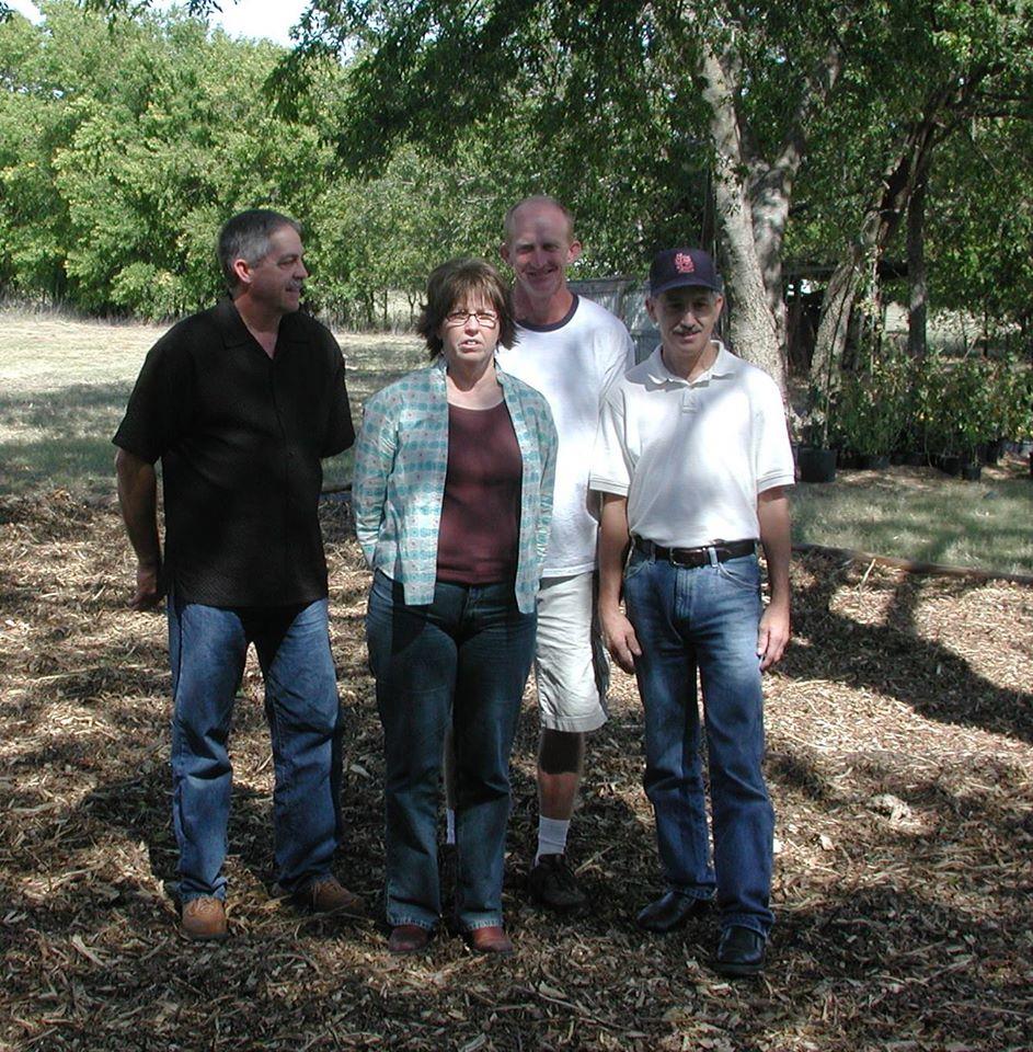 Four adults stand together in a sunny outdoor setting, enjoying a relaxed moment.