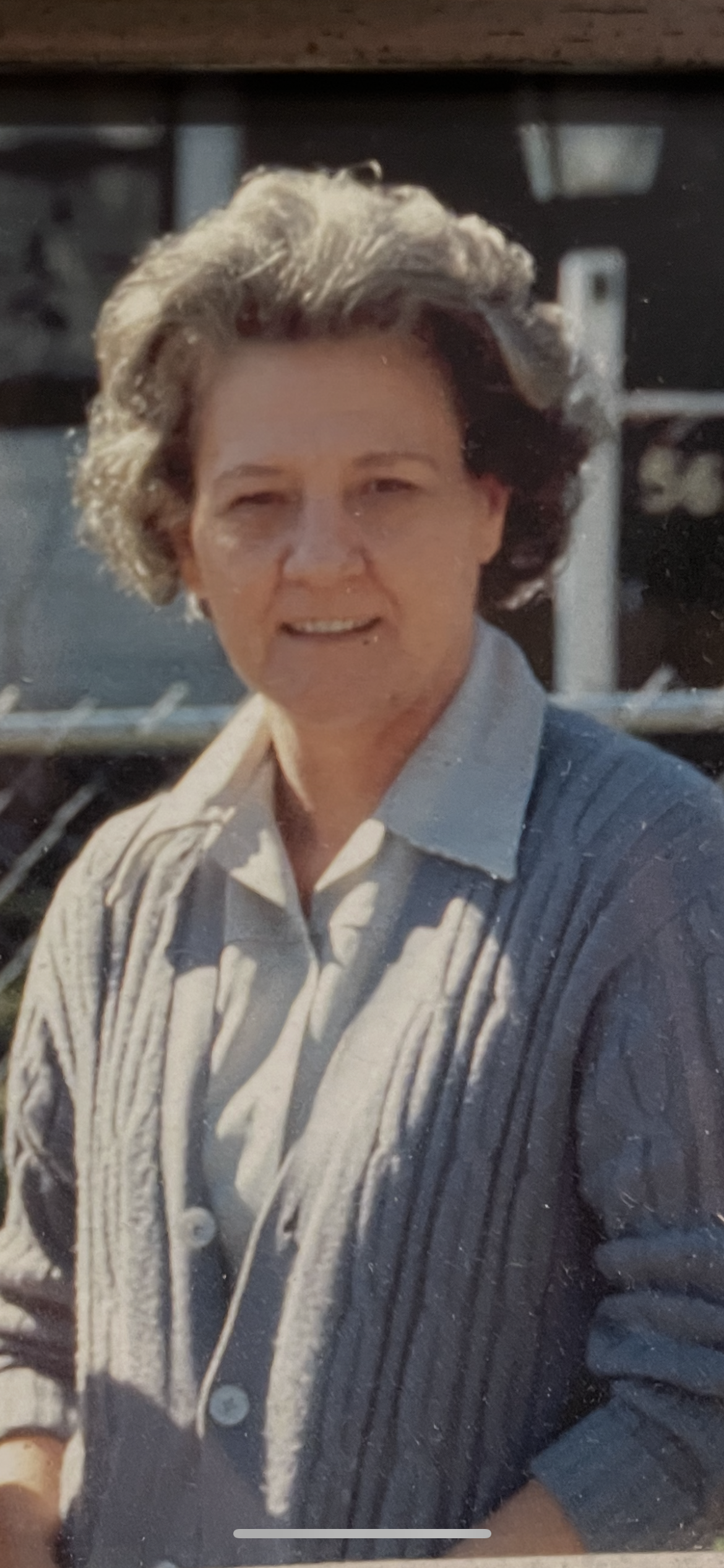 A joyful elderly woman stands outside, wearing a warm sweater and enjoying a bright day.