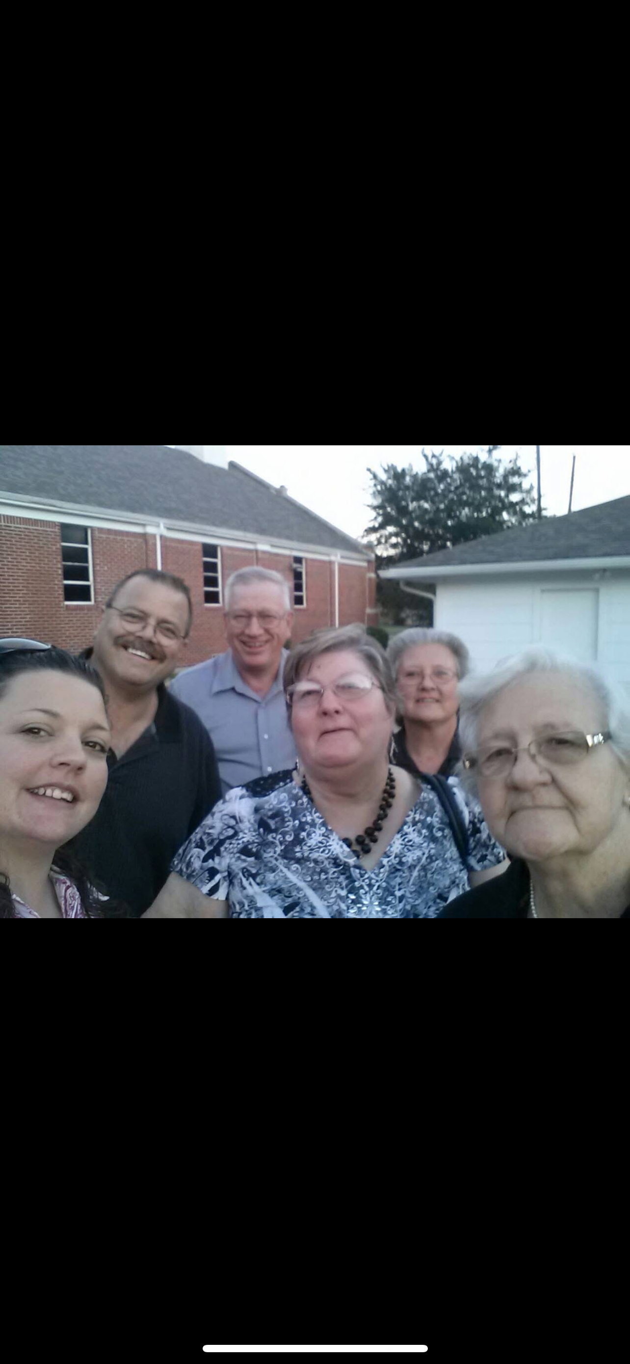 A group of friends stands together, smiling, during a reunion outside in the evening light.