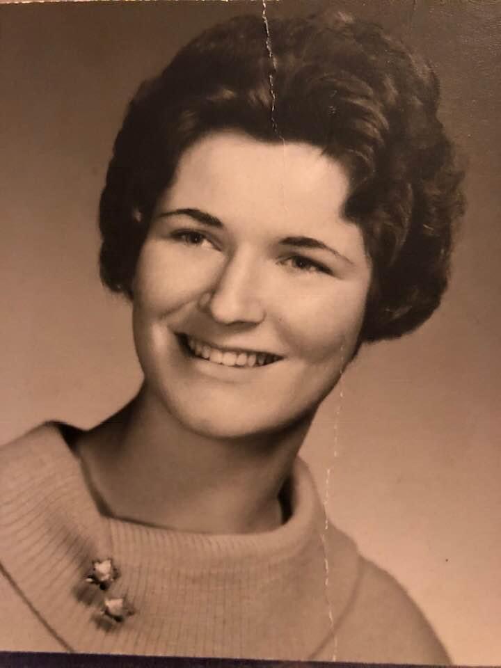 A young woman with curly hair smiles in a cozy sweater, embodying a classic portrait style.