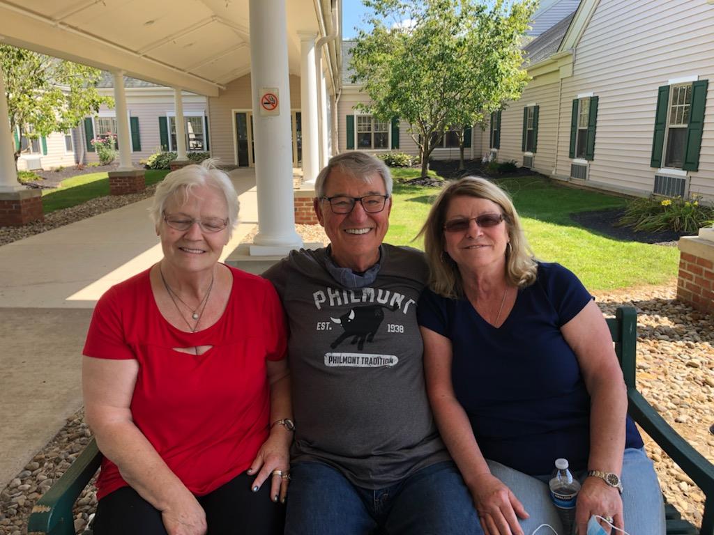Three seniors share laughter and conversation while sitting on a bench outdoors.