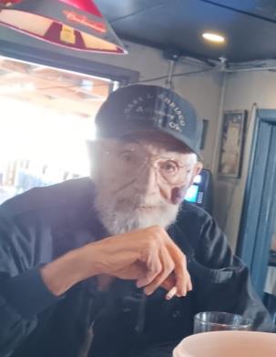 An elderly man sits at a diner, looking relaxed as he enjoys a cigarette and a drink.