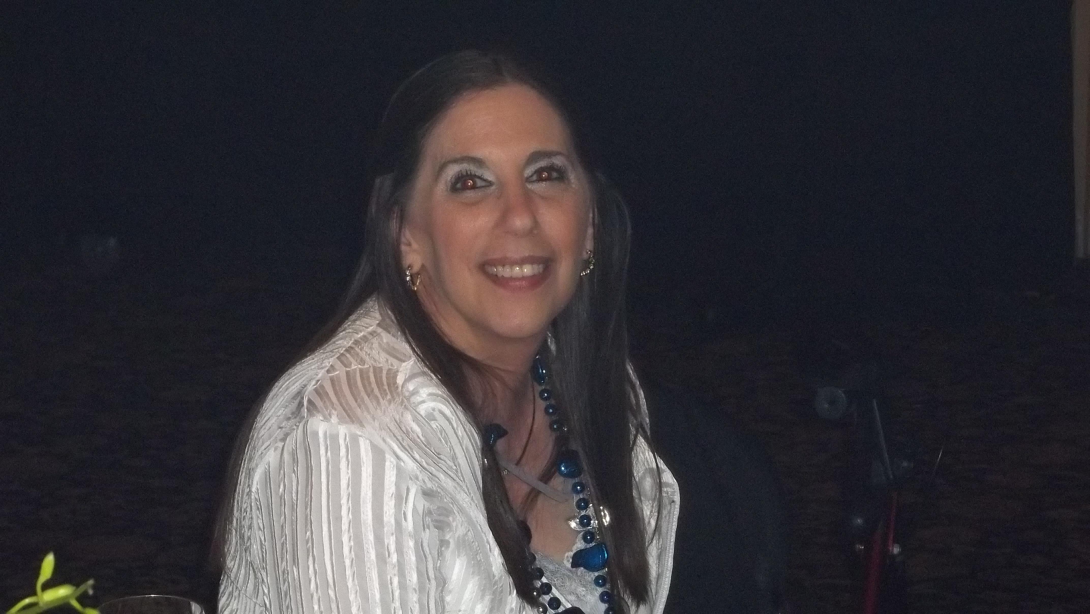A woman with long hair smiles brightly during an evening gathering, showcasing her accessories.