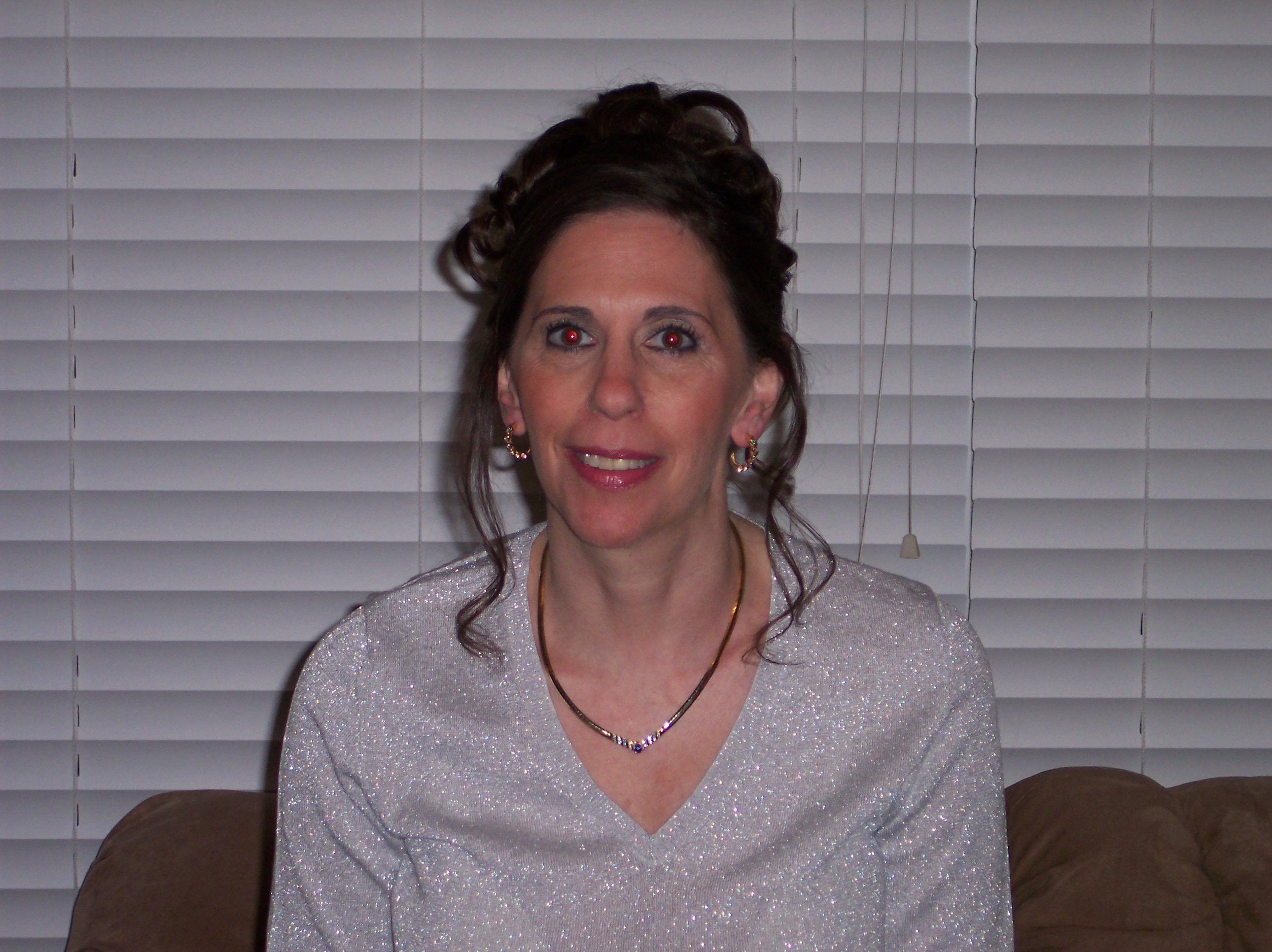 A woman with curly hair and sparkling attire smiles in a cozy living room setting.