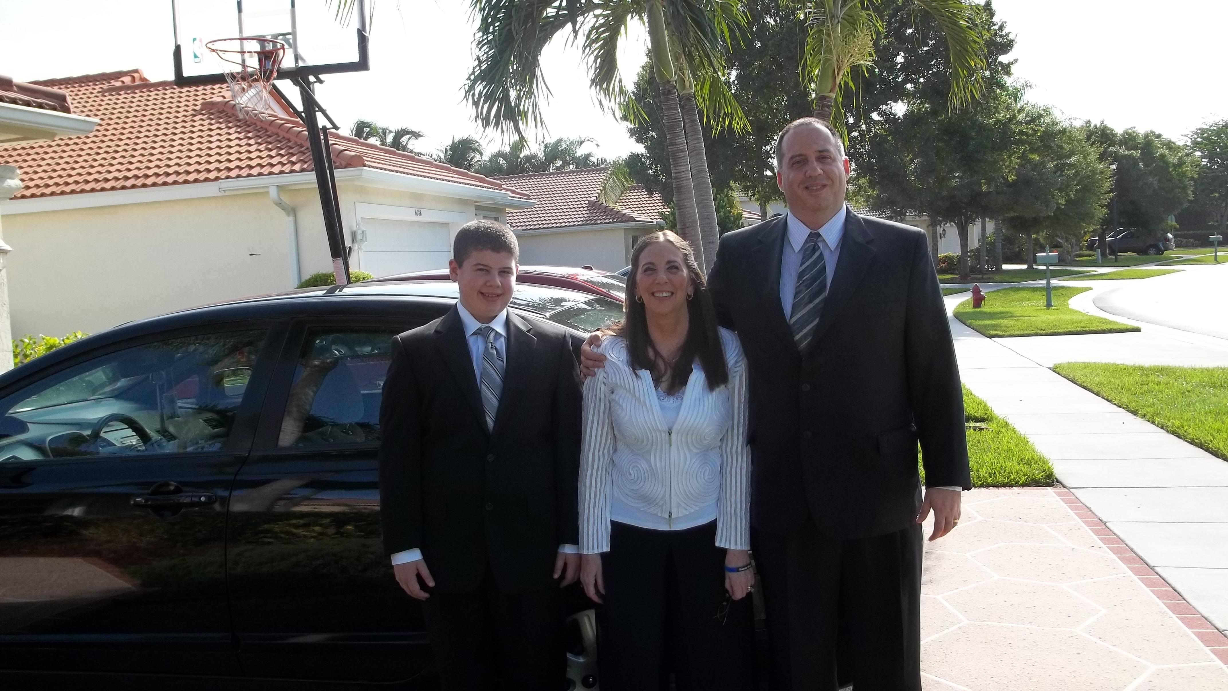Group of three people smiles while wearing formal clothing outside a suburban house.