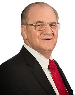 A confident senior man poses with a friendly smile in formal attire featuring a red tie.