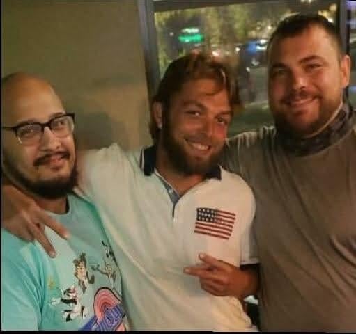 Three friends stand together, smiling and posing cheerfully at a bar in the evening atmosphere.