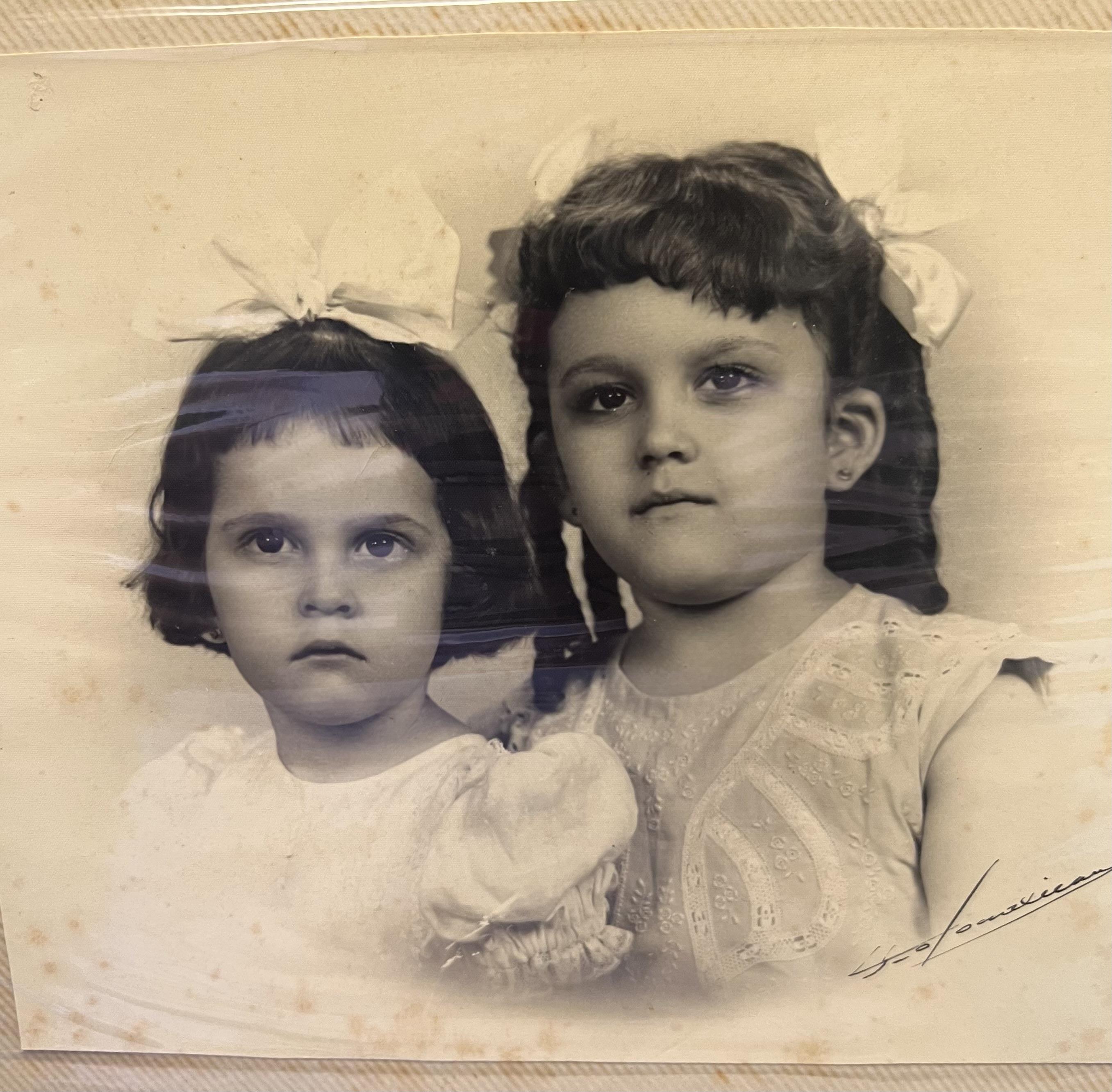 Two sisters with bows gaze at the camera, capturing a moment of childhood connection.