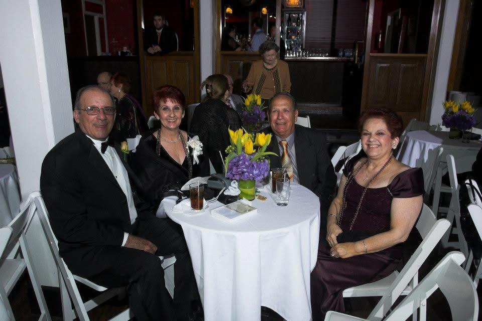 Guests in formal attire gather around flower-adorned tables, enjoying the evening.
